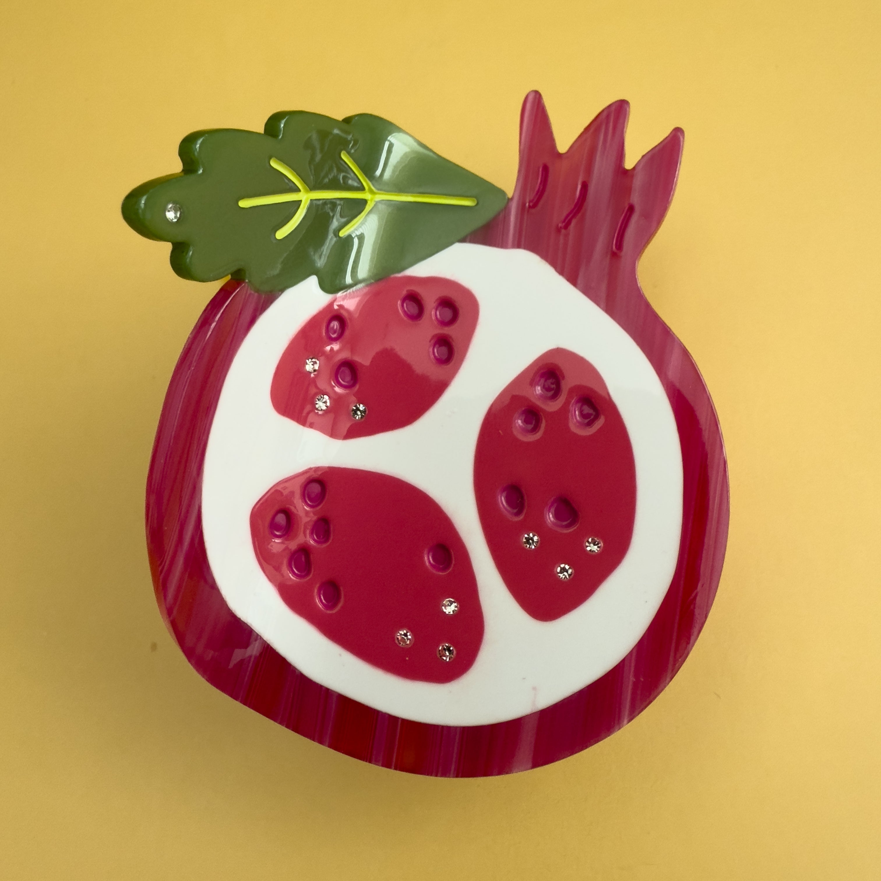 Decorative pomegranate hair claw with a green leaf. Don't let this tough exterior fool you! Beneath its rosy glow lies a treasure chest of tiny, ruby-red jewels, each one a delightful explosion of sweet-tart goodness.

Pomegranate hair claw season is here and we can help but wearing it too!