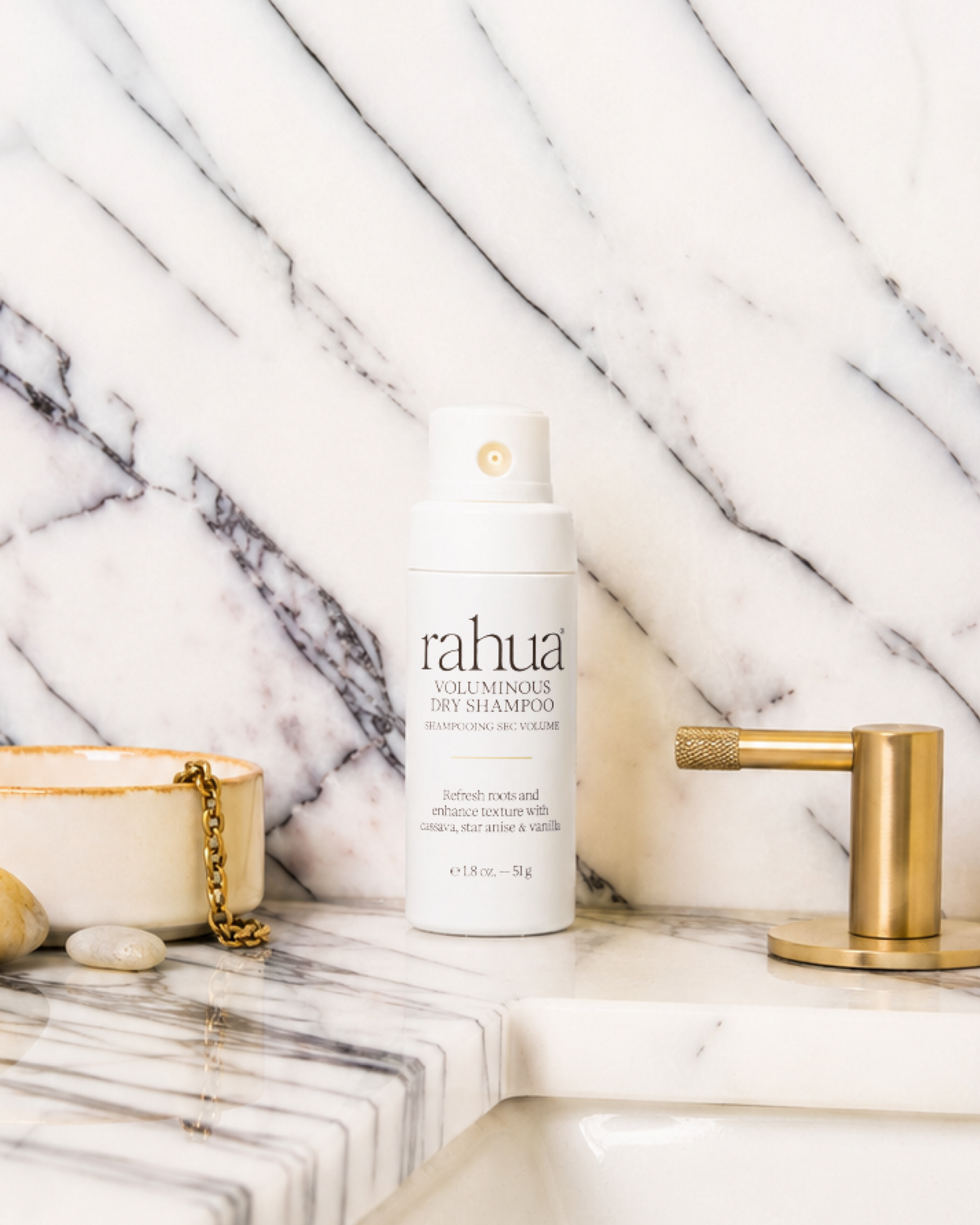 Bottle of rahua shampoo on a marble surface with a candle and faucet.