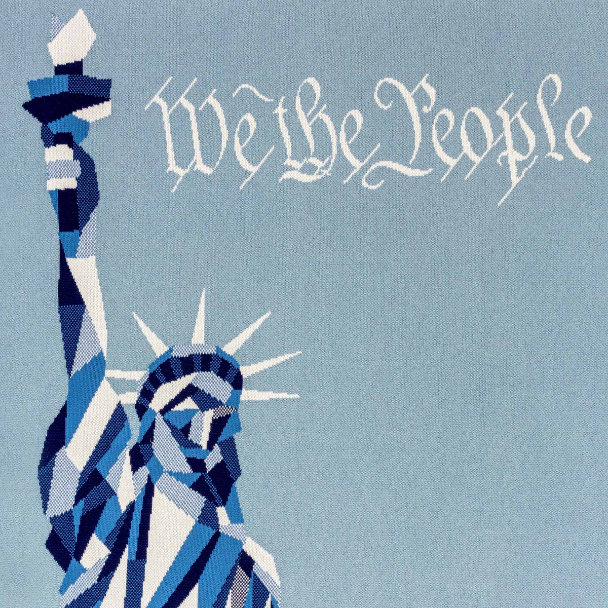 Introducing the “Statue of Liberty | We the People” Cotton Sustainable Knit Modern Throw Blanket by in2green—featuring a stylized blue illustration of the Statue of Liberty’s upper half and the phrase “We the People” in white script on a light blue background. This patriotic throw from in2green is perfect for celebrating American identity with both style and sustainability.