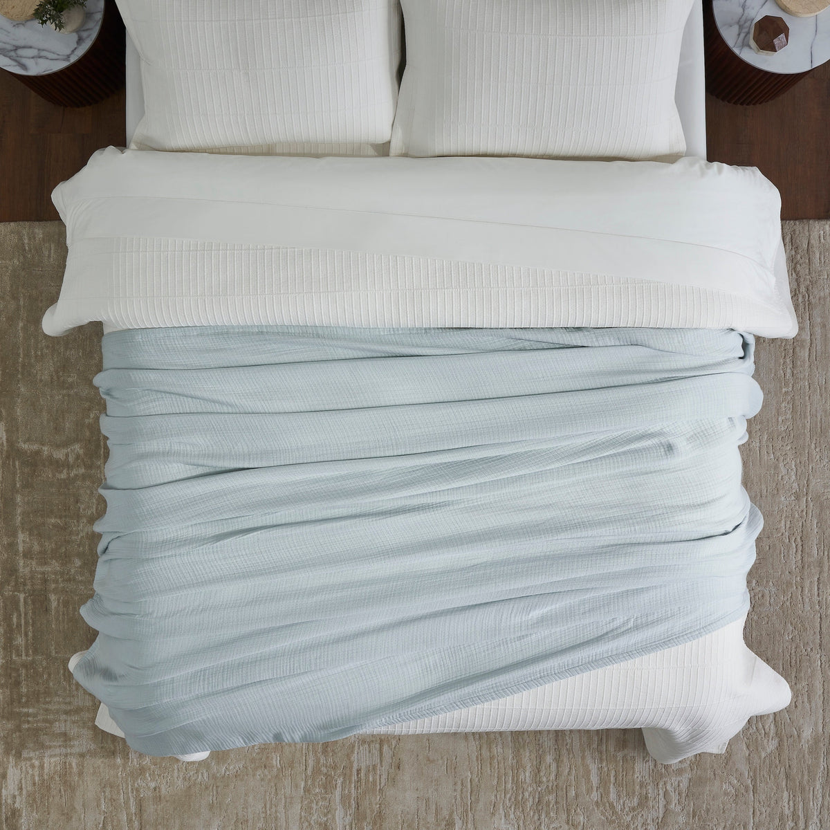 BL-863-11096_4|Overhead view showcasing a luxurious light blue textured muslin blanket folded neatly on a pristine white bed.