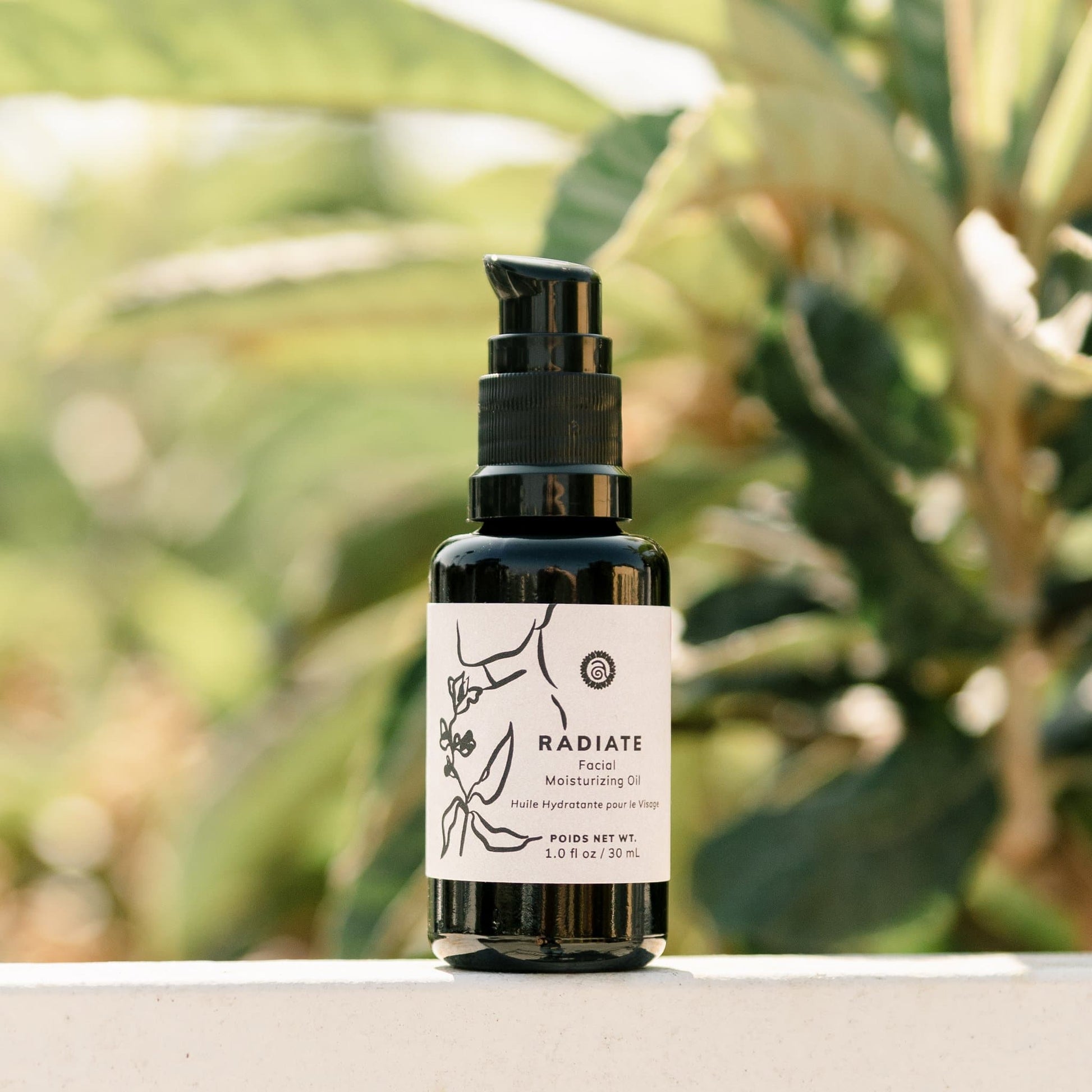 Radiate Facial Moisturizing Oil in a dark glass pump bottle displayed outdoors with soft greenery in the background.