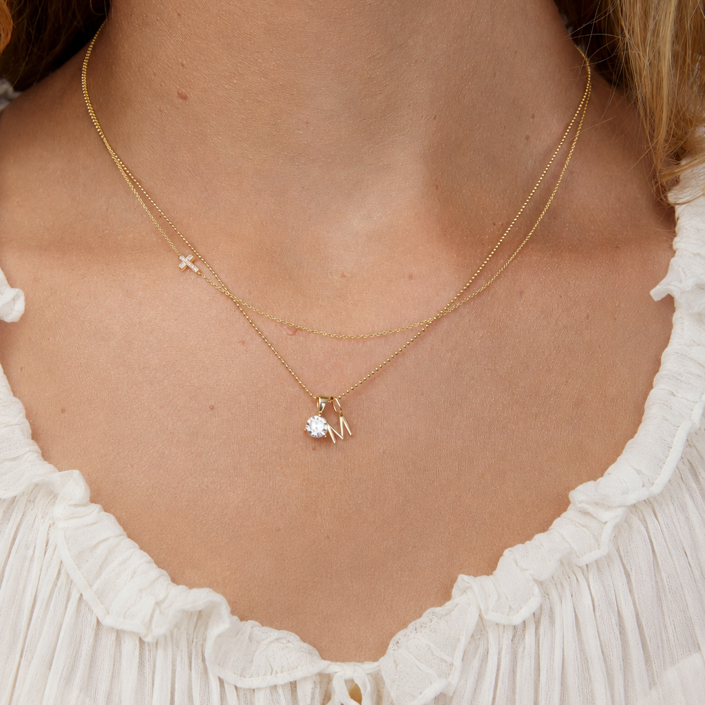 Necklace with a small gold letter pendant worn by a person in a white dress