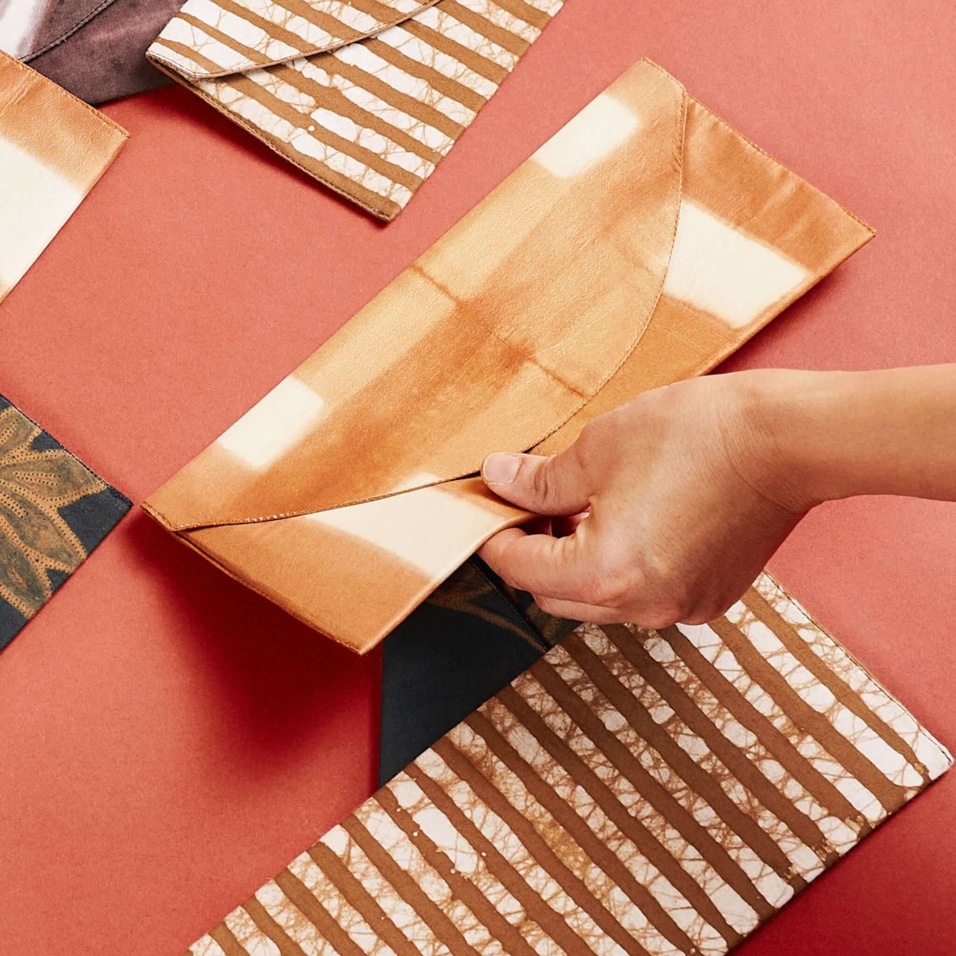 Melo Gold Mulberry Silk Shibori Hand Crafted Envelope Pouch being held, showcasing its unique design and artisan craftsmanship.