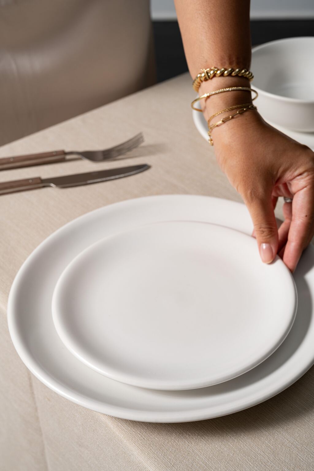 Hand placing a ceramic bowl on stacked stoneware plates in Hamkke Home’s Bone glaze, styled on a neutral table setting with cutlery.