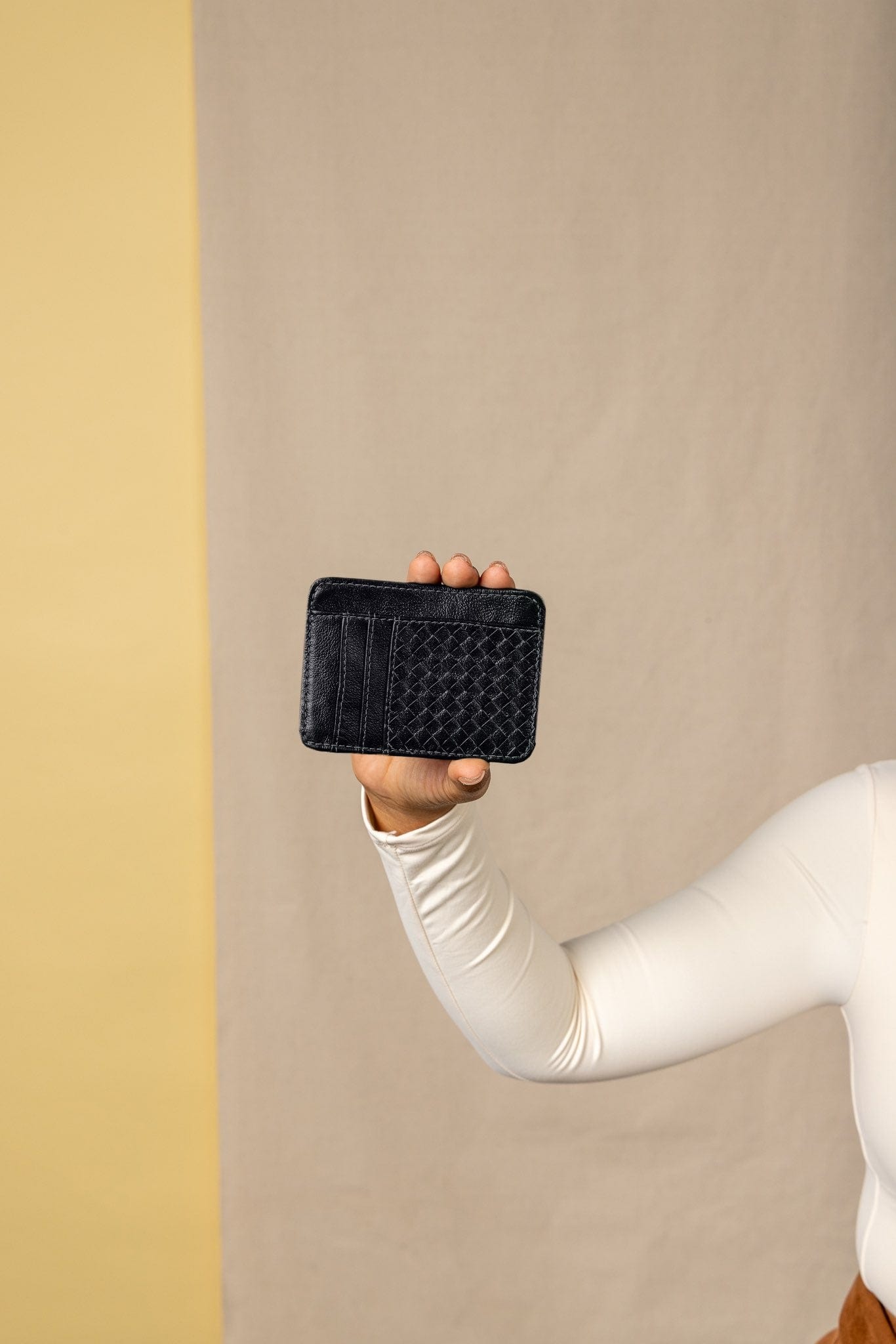 Person holding a black woven wallet against a beige background