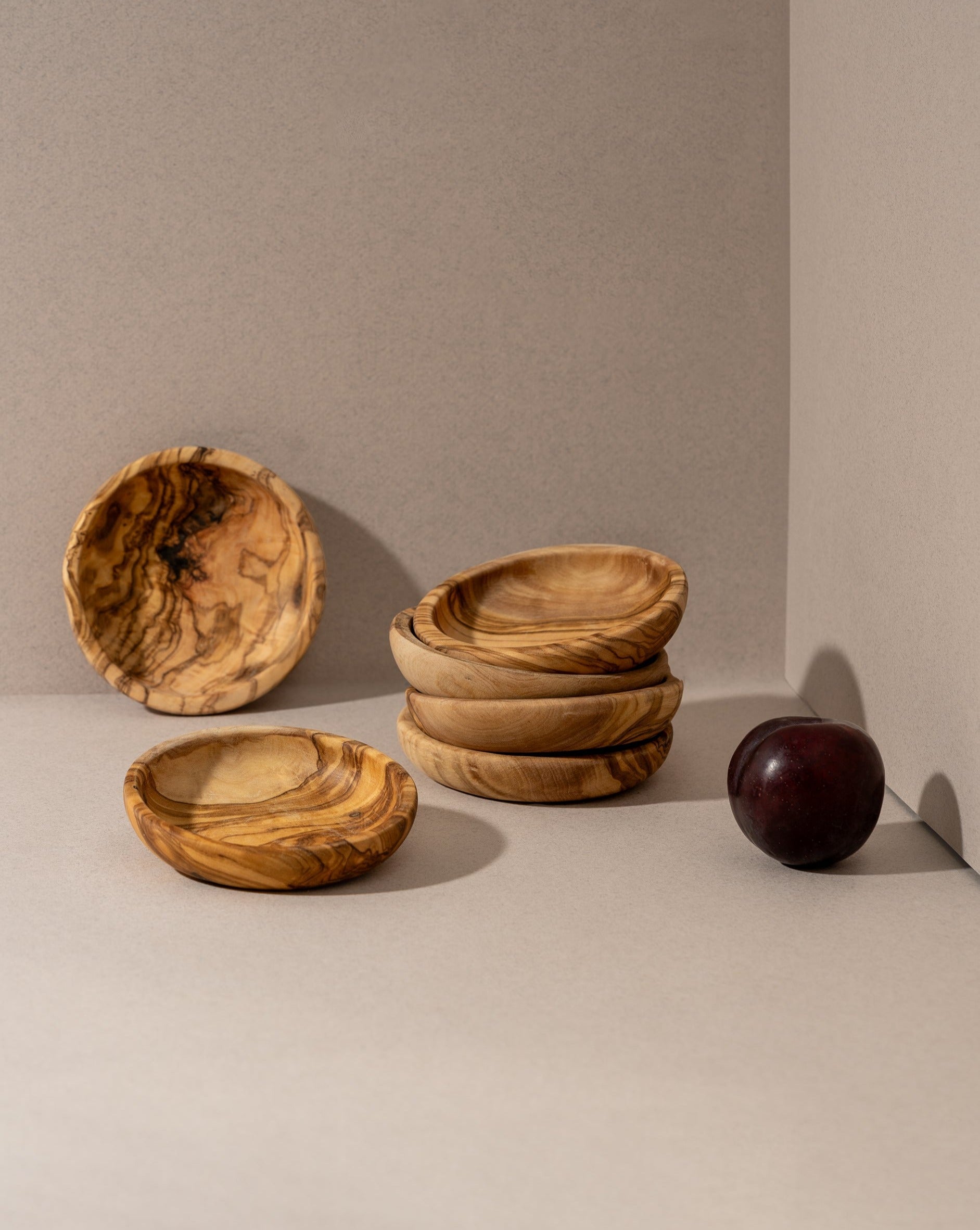 Stacked natural olive wood ramkins on a neutral background, with a shadow falling across the image, highlighting the rustic and handmade aesthetic of the bowls.