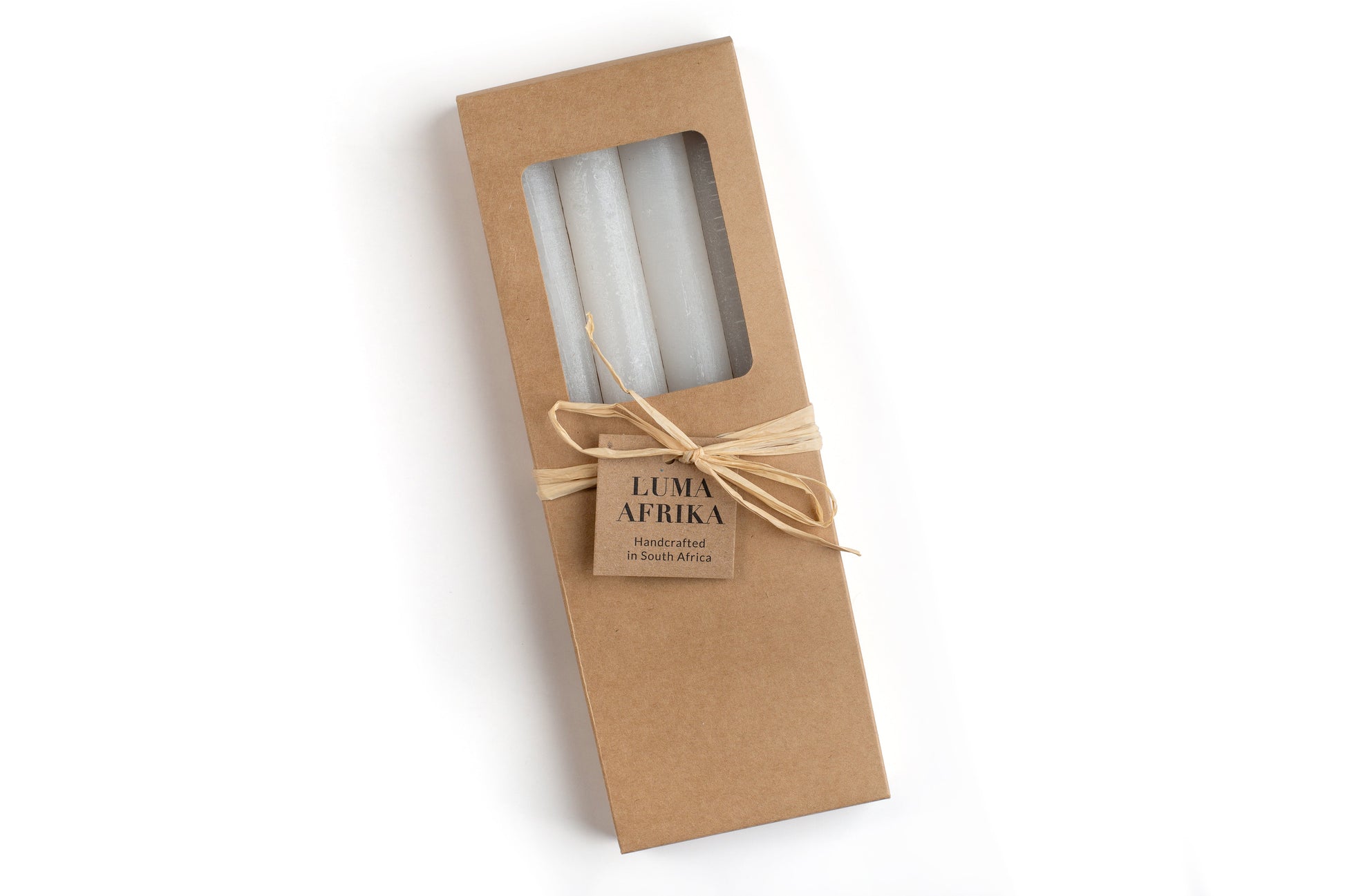 4 white frosted tapers in a kraft bown gift box, ties with raffia and a story card. Luma Afrika. Fair Trade.