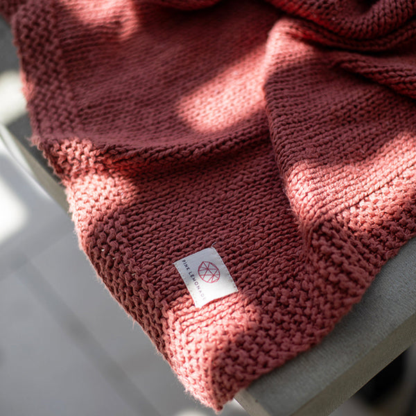 Red-rust rosewood organic cotton blanket with a Pink Lemonade brand label in the corner.