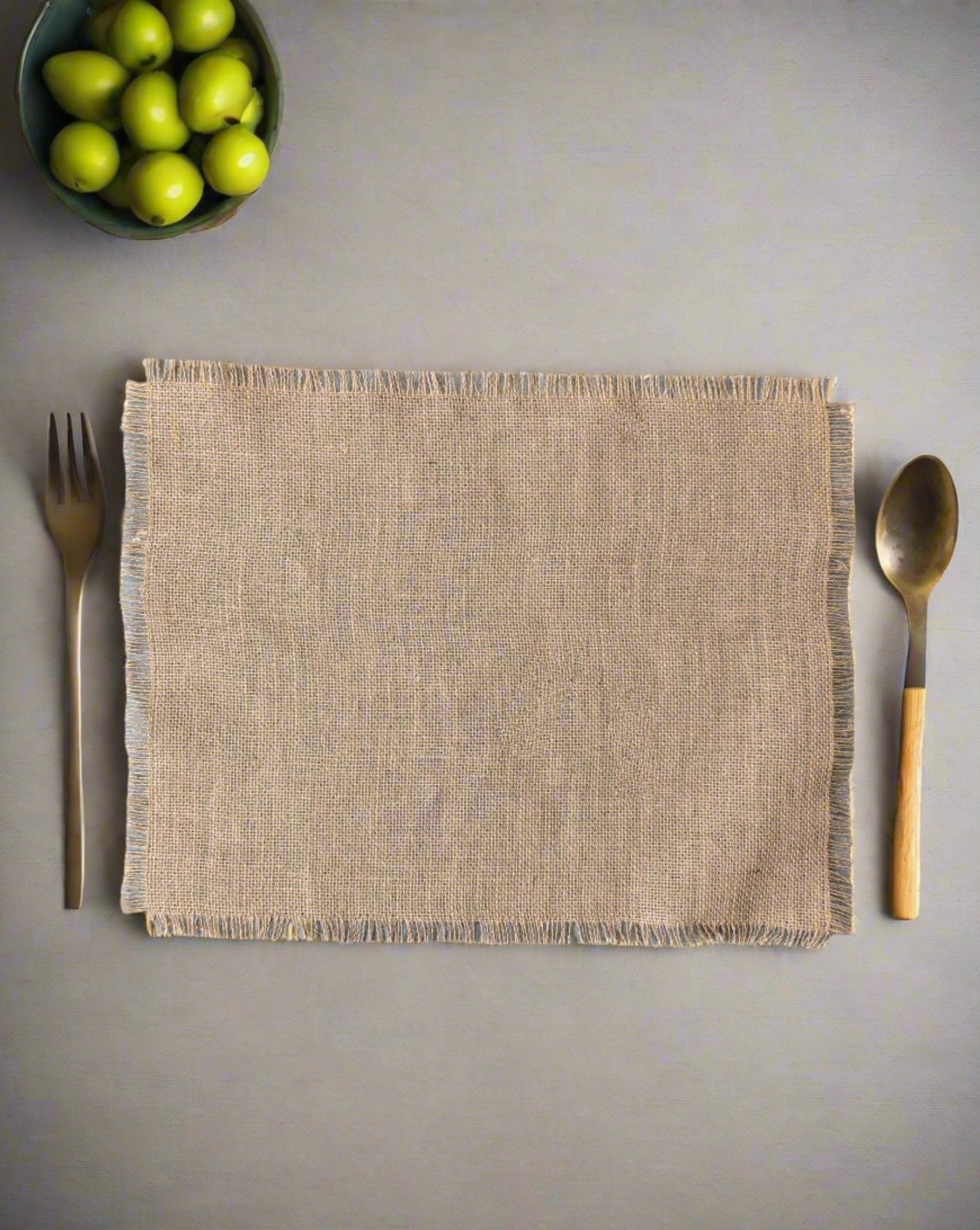 A beige burlap placemat on a gray surface with a fork on the left side and a spoon on the right side, both with wooden handles.