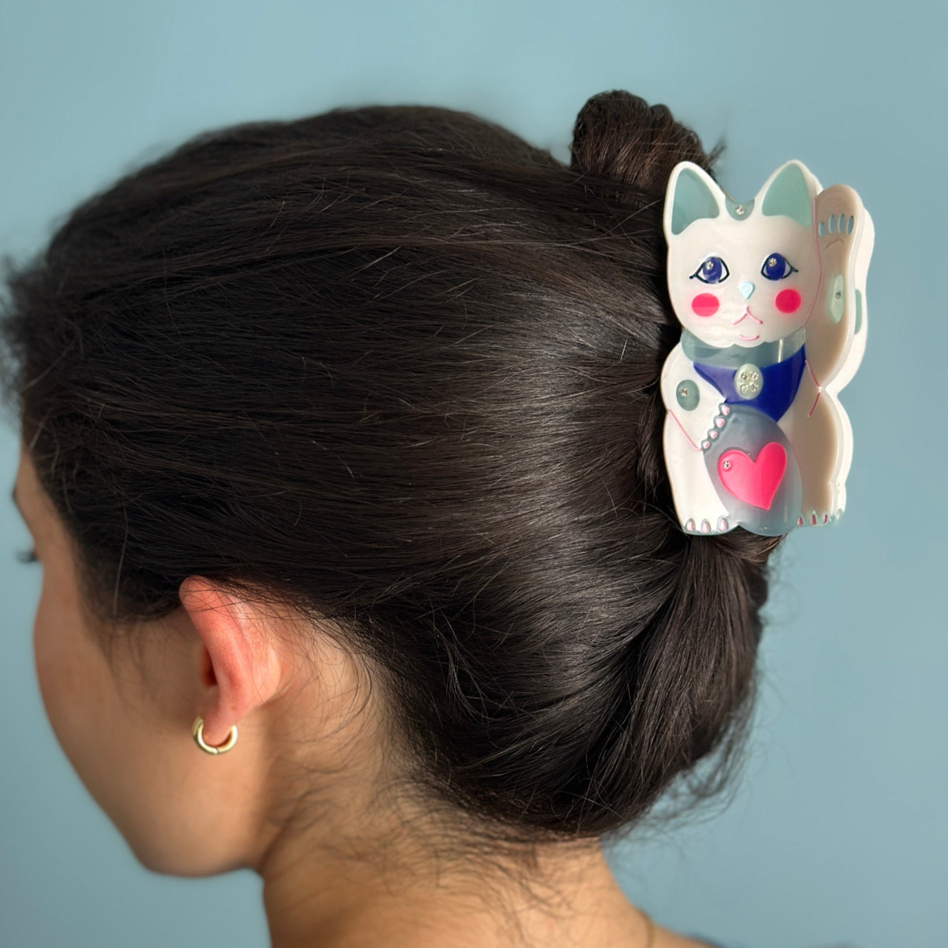 A maneki-neko white cat hair claw with a pink heart from Centinelle. Handmade on cellulose acetate, with splice technique, exquisite miniature details and crystals, that are tied directly to its value and make them unique and special. 