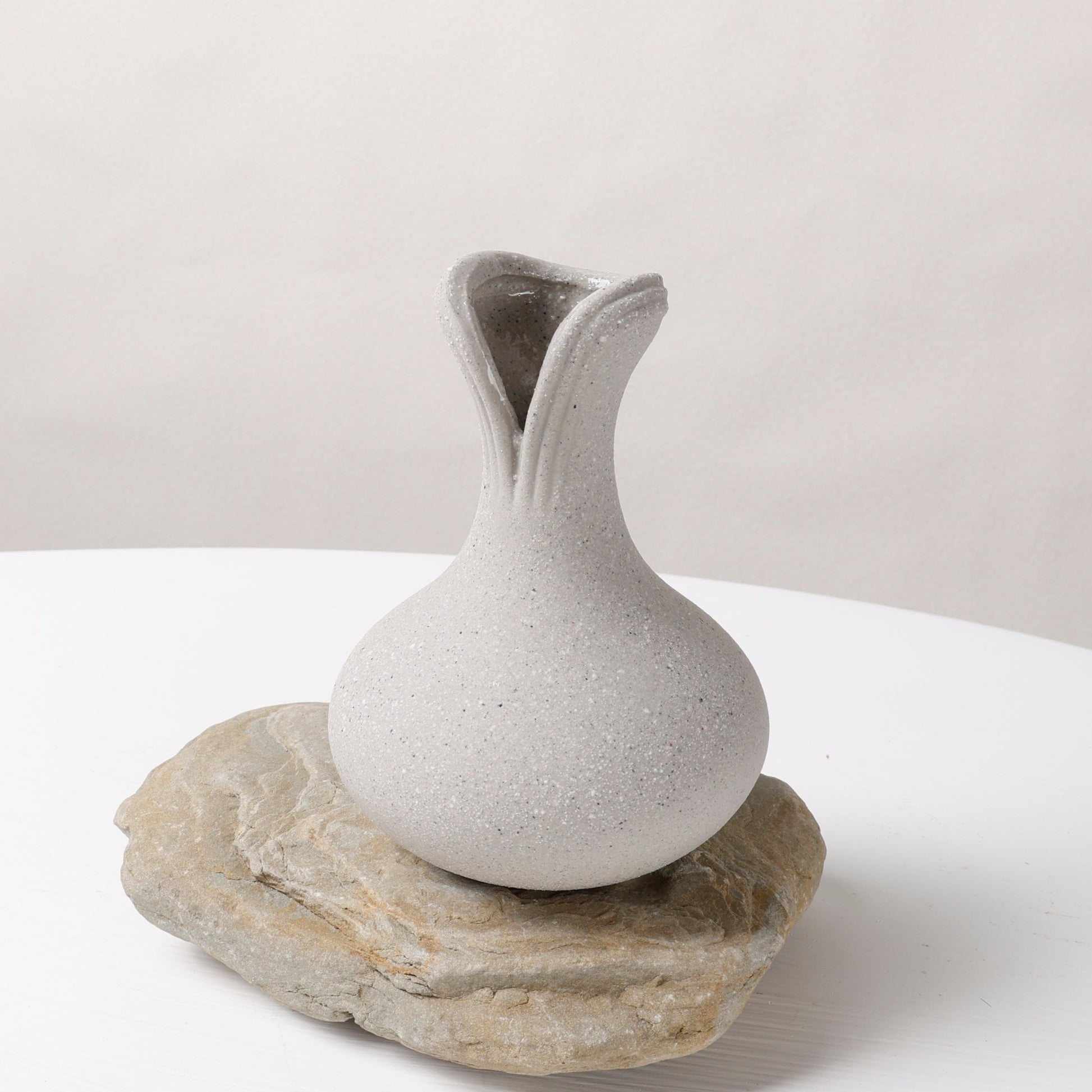 White ceramic vase on a natural stone base against a plain background