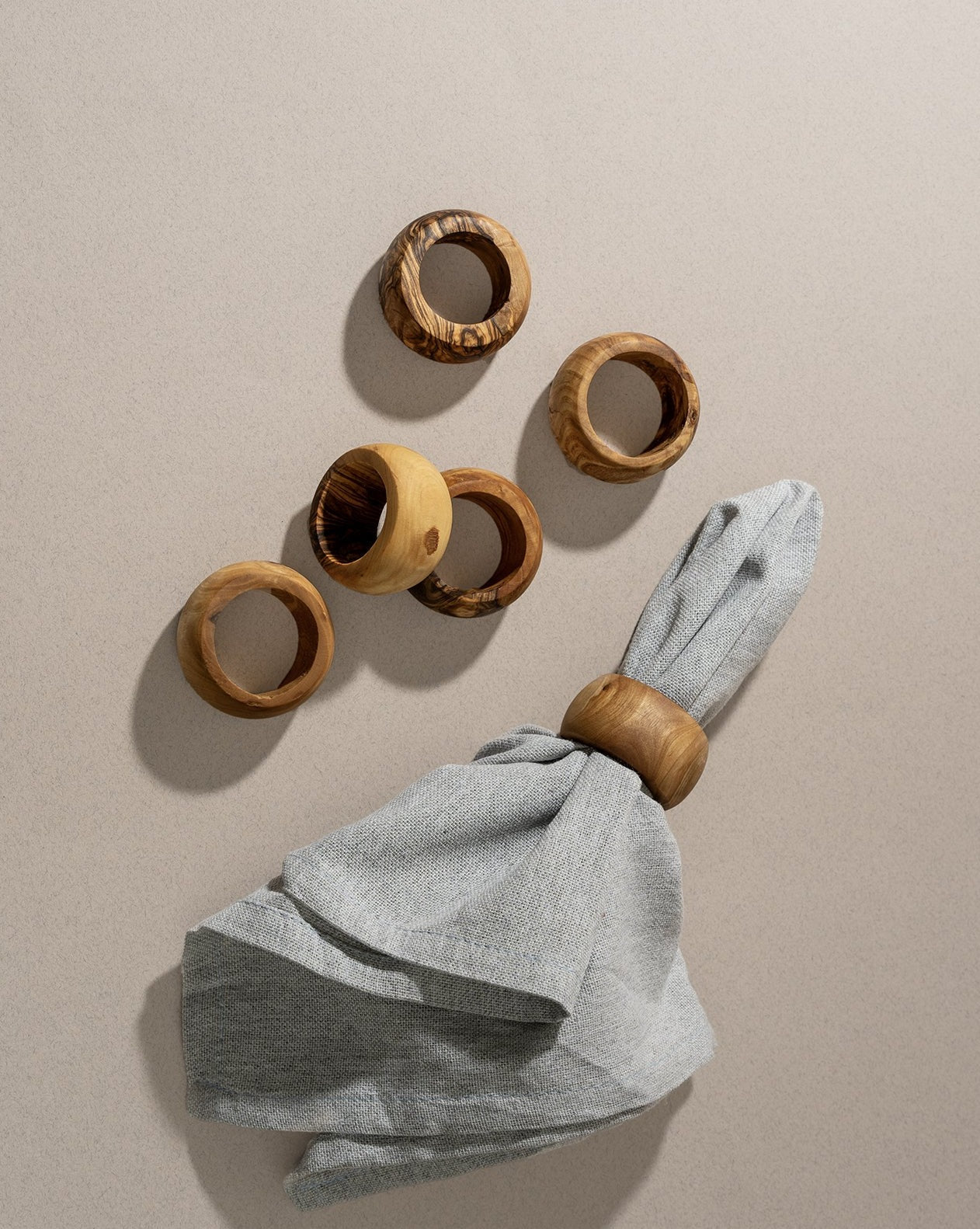 A set of olive wood napkin rings displayed on a neutral surface, with one ring holding a neatly folded cloth napkin as a sample.