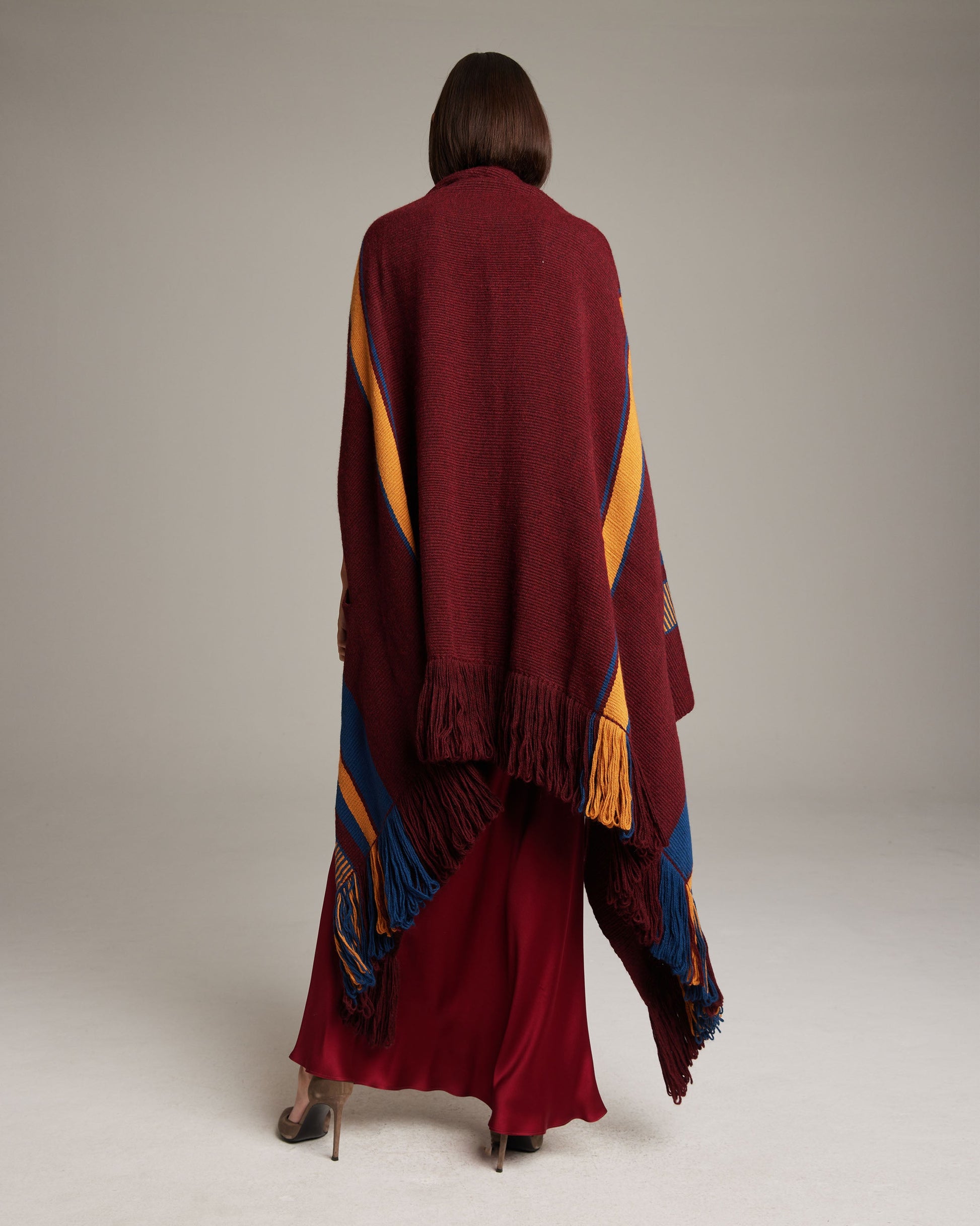 Model wearing a Cascade Wrap in Baby Alpaca, showcasing the back view with burgundy, orange, and blue colors.
