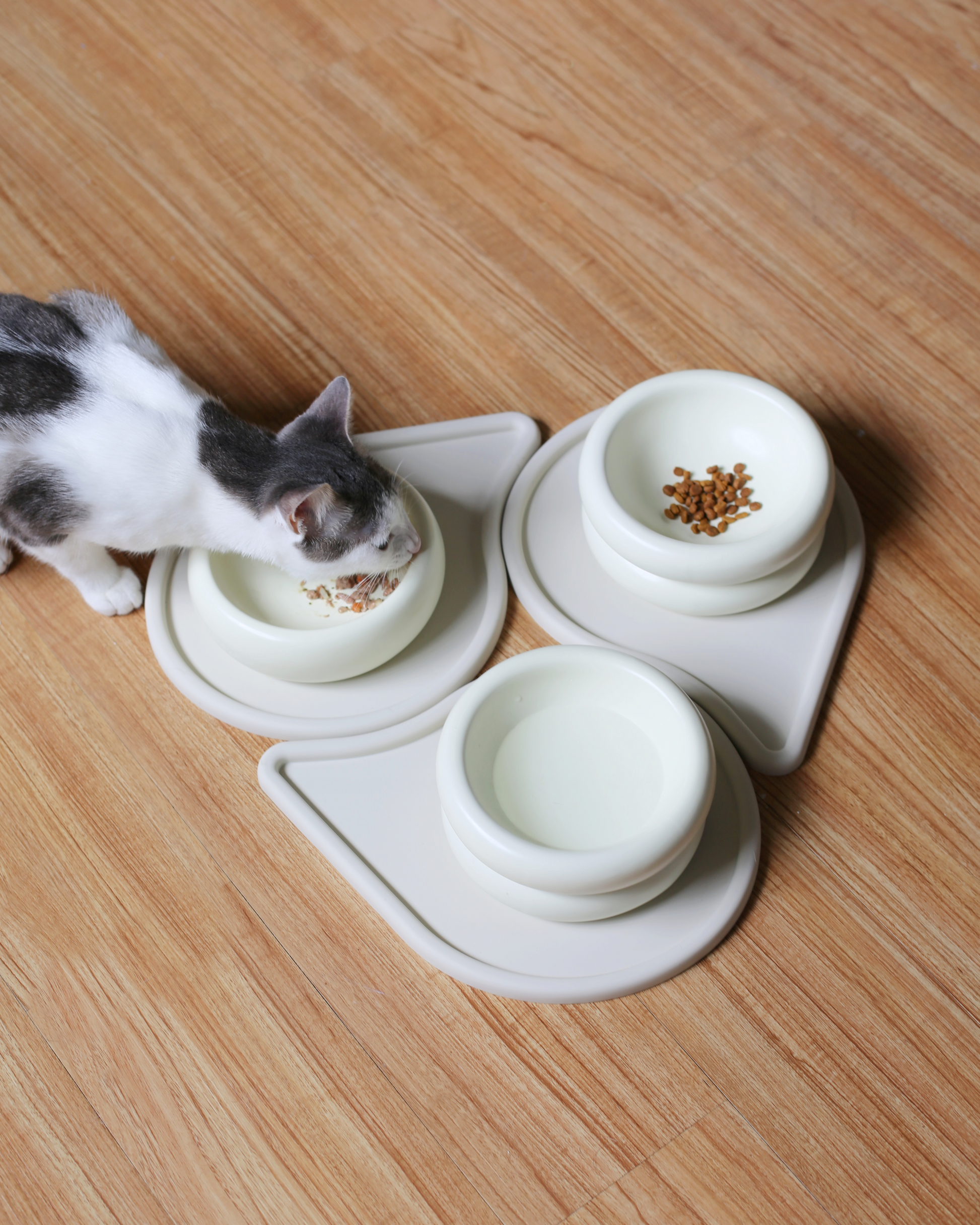 three raindrop shaped pet feeding mat by catenary home modern cat furniture company that can be used as a cat food mat and dog food mat or pet meal mat that tesselate interlock and interweave to create all types of patterns with aesthetic cat eating from cat food bowls and raised cat bowls with food and water in them on hardwood floors