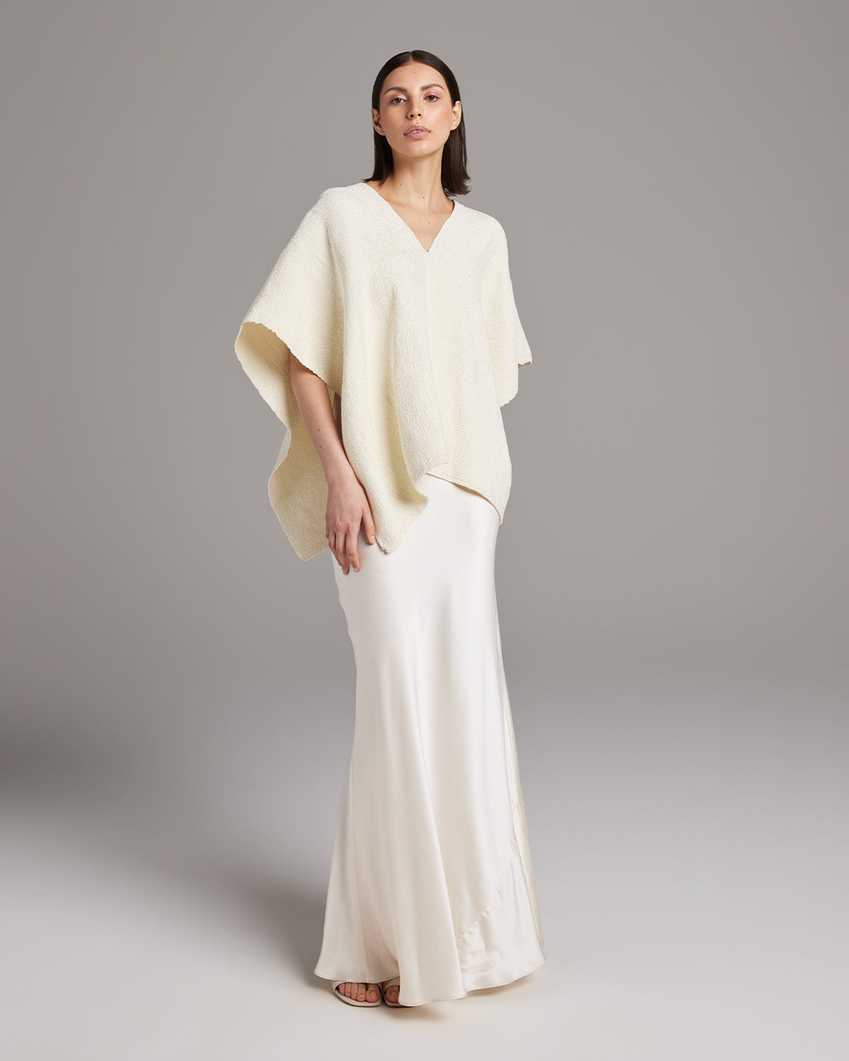 Model wearing a cream Manta Captiva poncho over a white skirt
