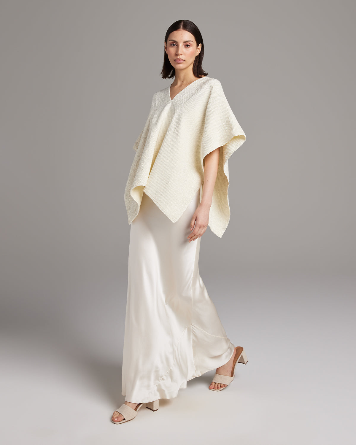 Model wearing a cream Manta Captiva poncho over a long white skirt