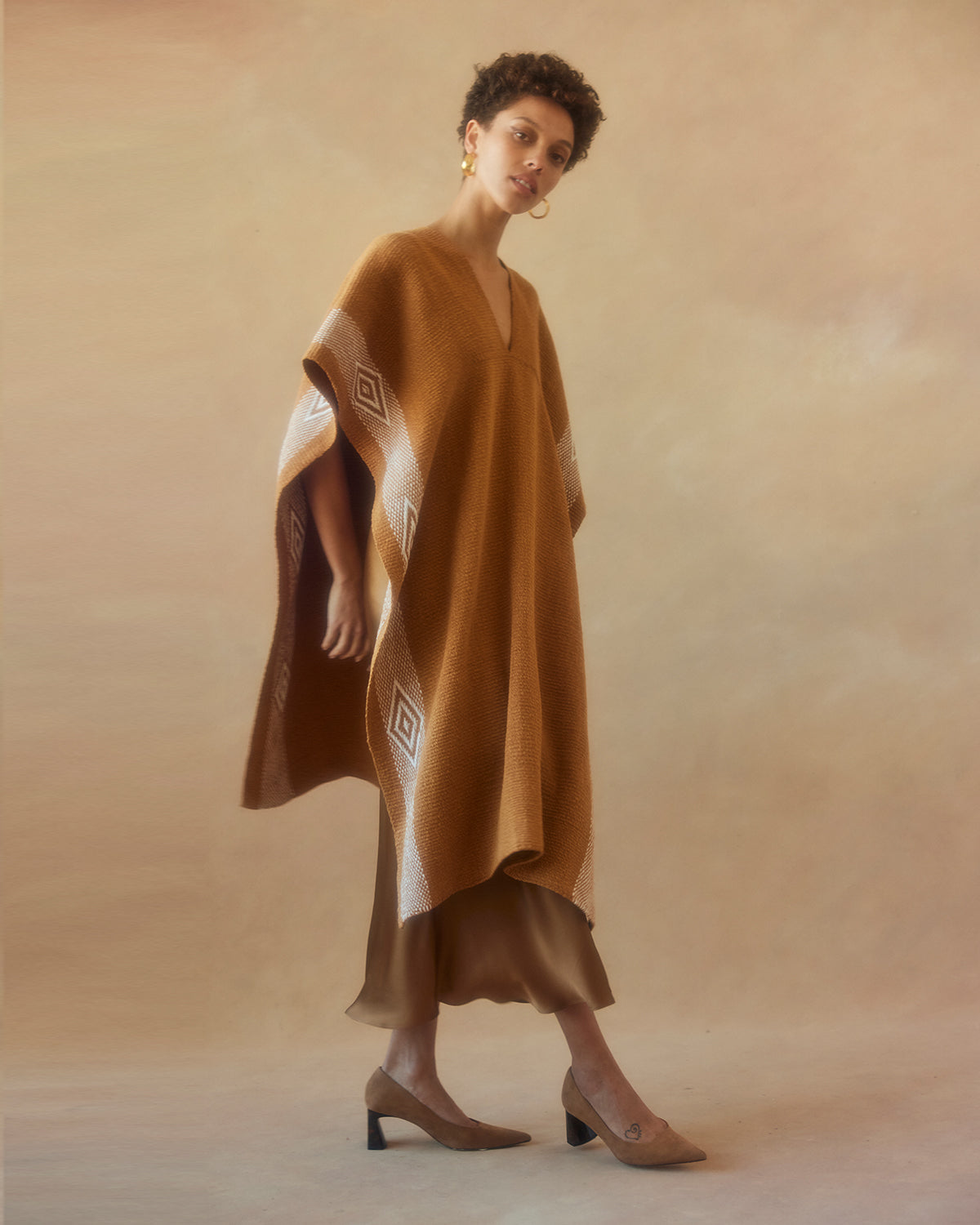 Model wearing a gold Manta Diamante poncho with a diamond pattern