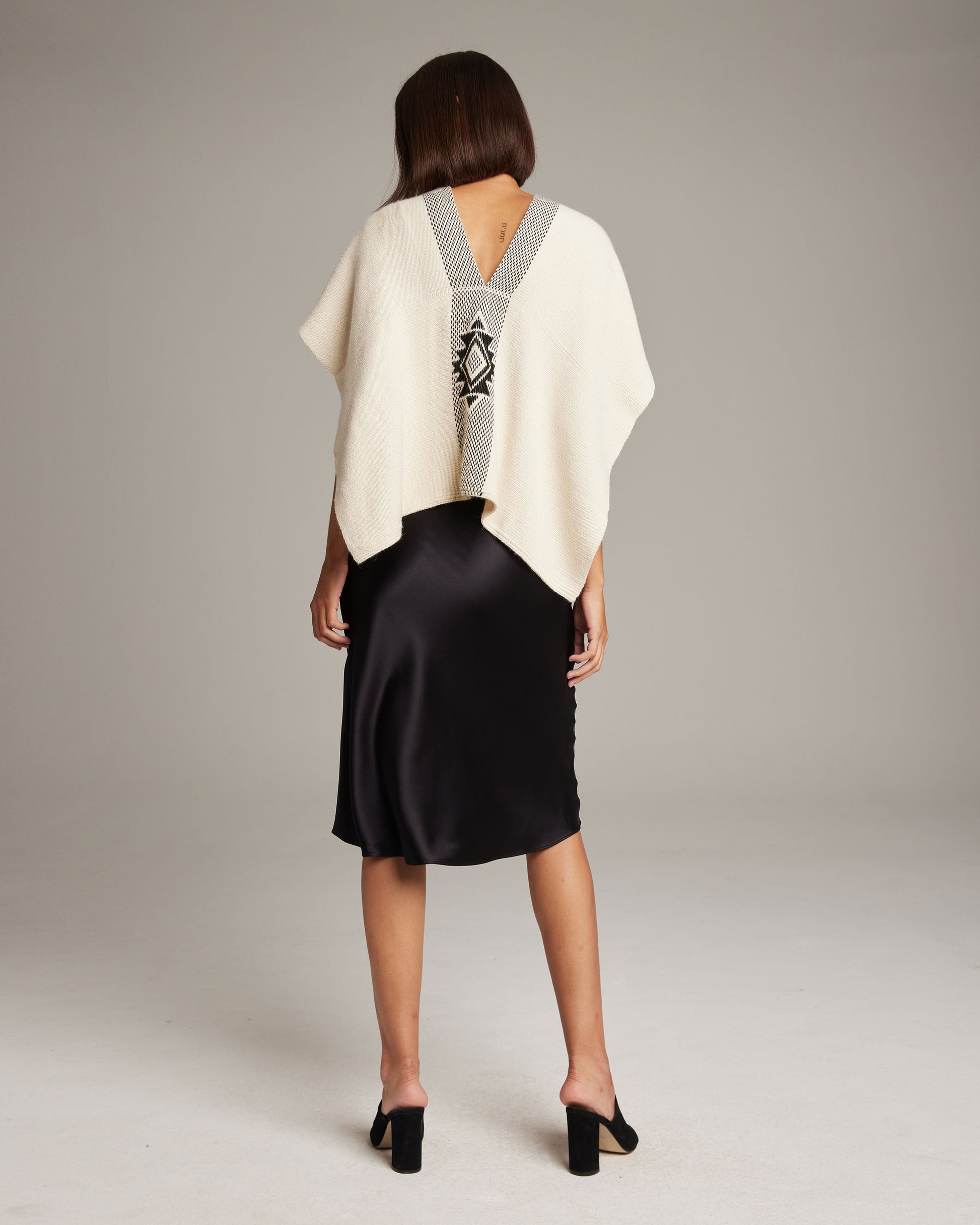 Back view of a woman wearing a hand-loomed ivory and black Manta Estrella poncho, showcasing the Estrella pattern.