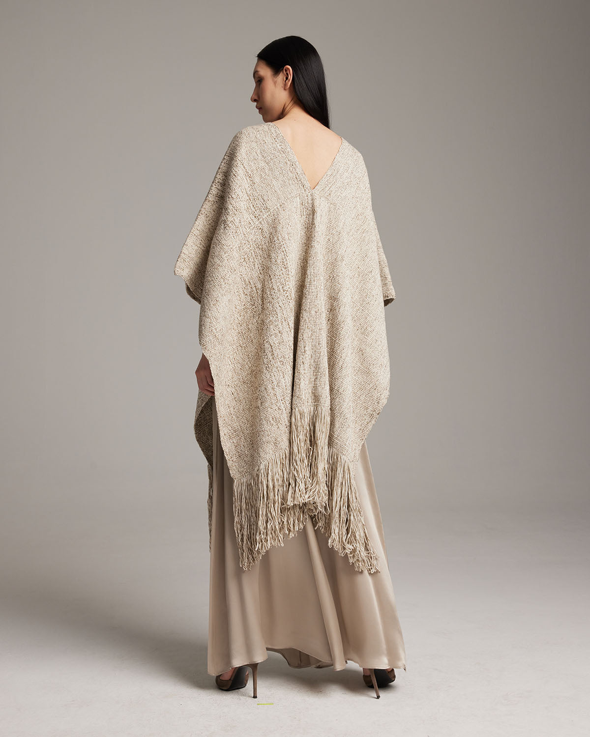Model wearing a long, hand-loomed sand-colored fringe manta with a V-neck design.