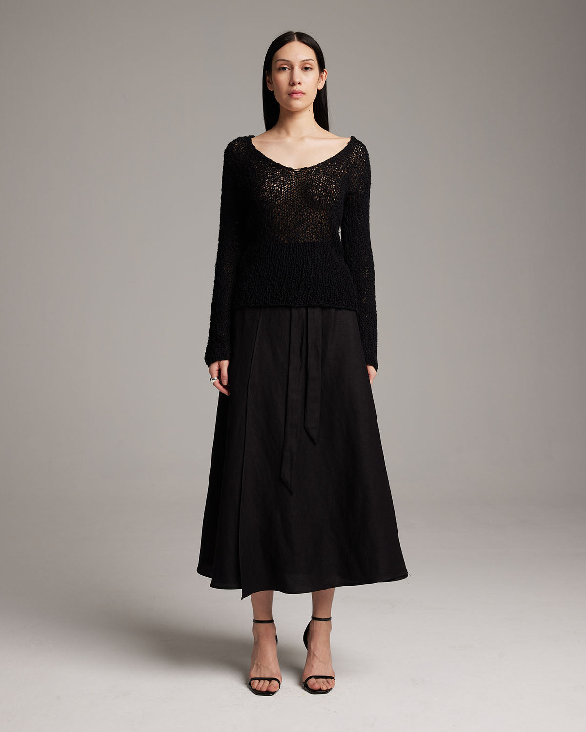Model wearing a black Flammé Loose Knit Long Sweater with a skirt and heels
