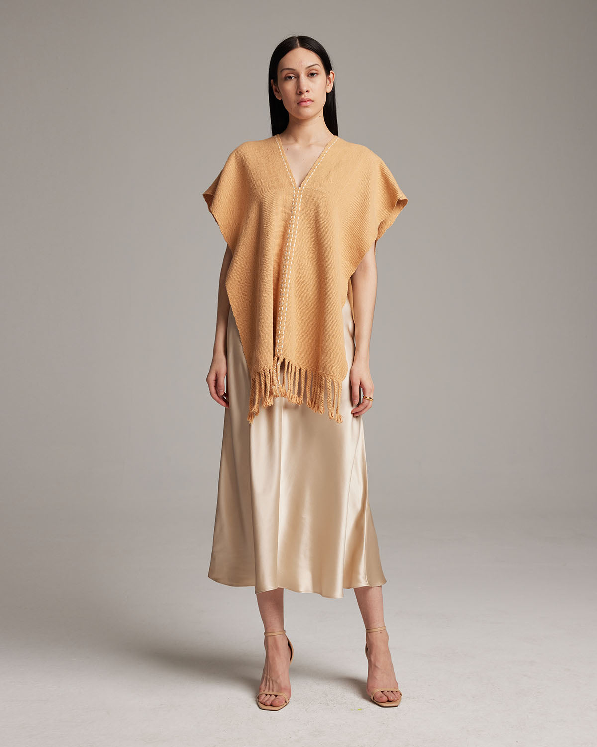 Model wearing a copper threads manta in apricot color, styled with a satin skirt.