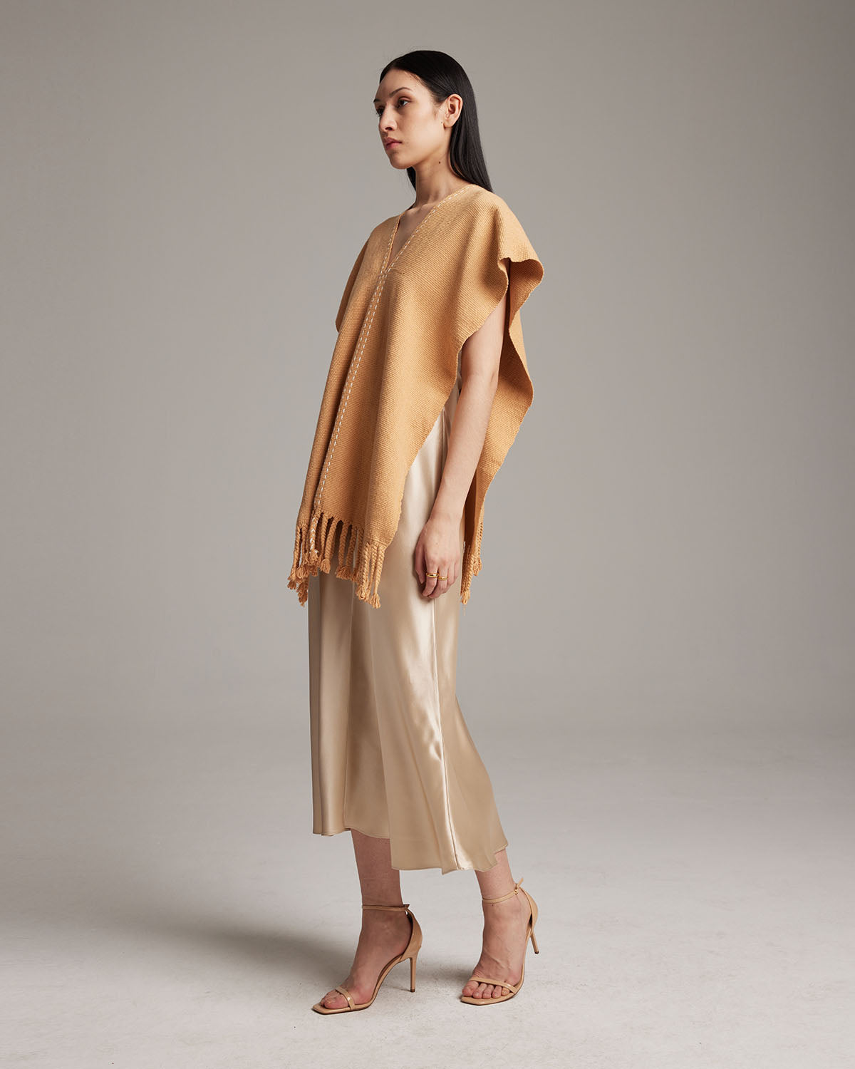 Model wearing a copper threads manta in apricot color, showcasing fringe detail.