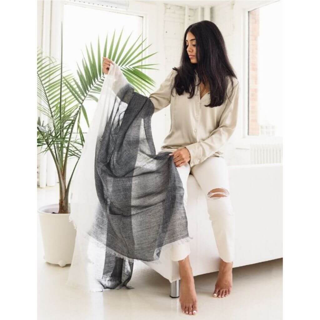 Model showcasing a Granite Black White Ombre Linen Silk Handloom Scarf in a bright, stylish setting with a green plant.