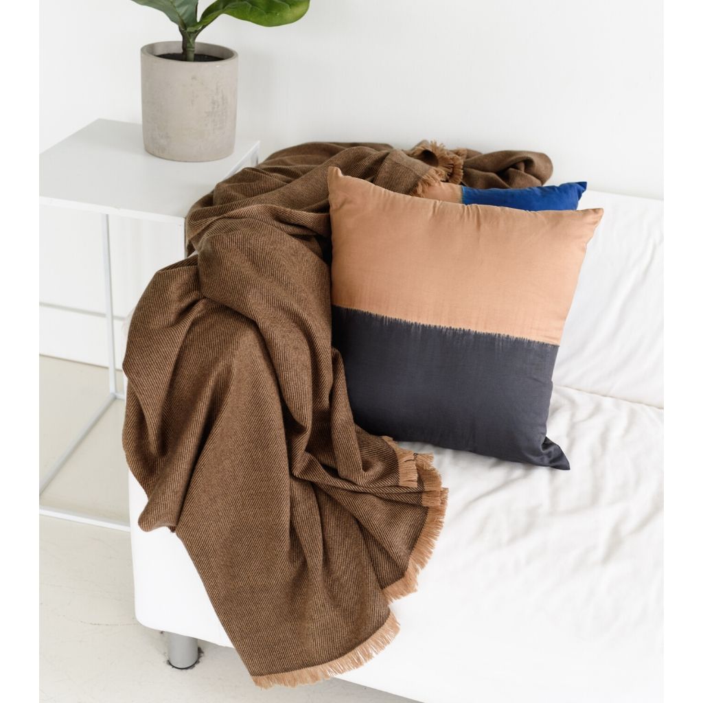 Kala Black & Gold Color Block Mulberry Silk Square Pillow with a cozy blanket on a modern sofa.