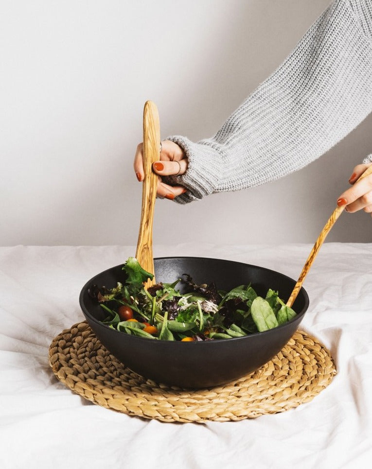 Natural olive wood spatula being used to mix a bowl of salad.
