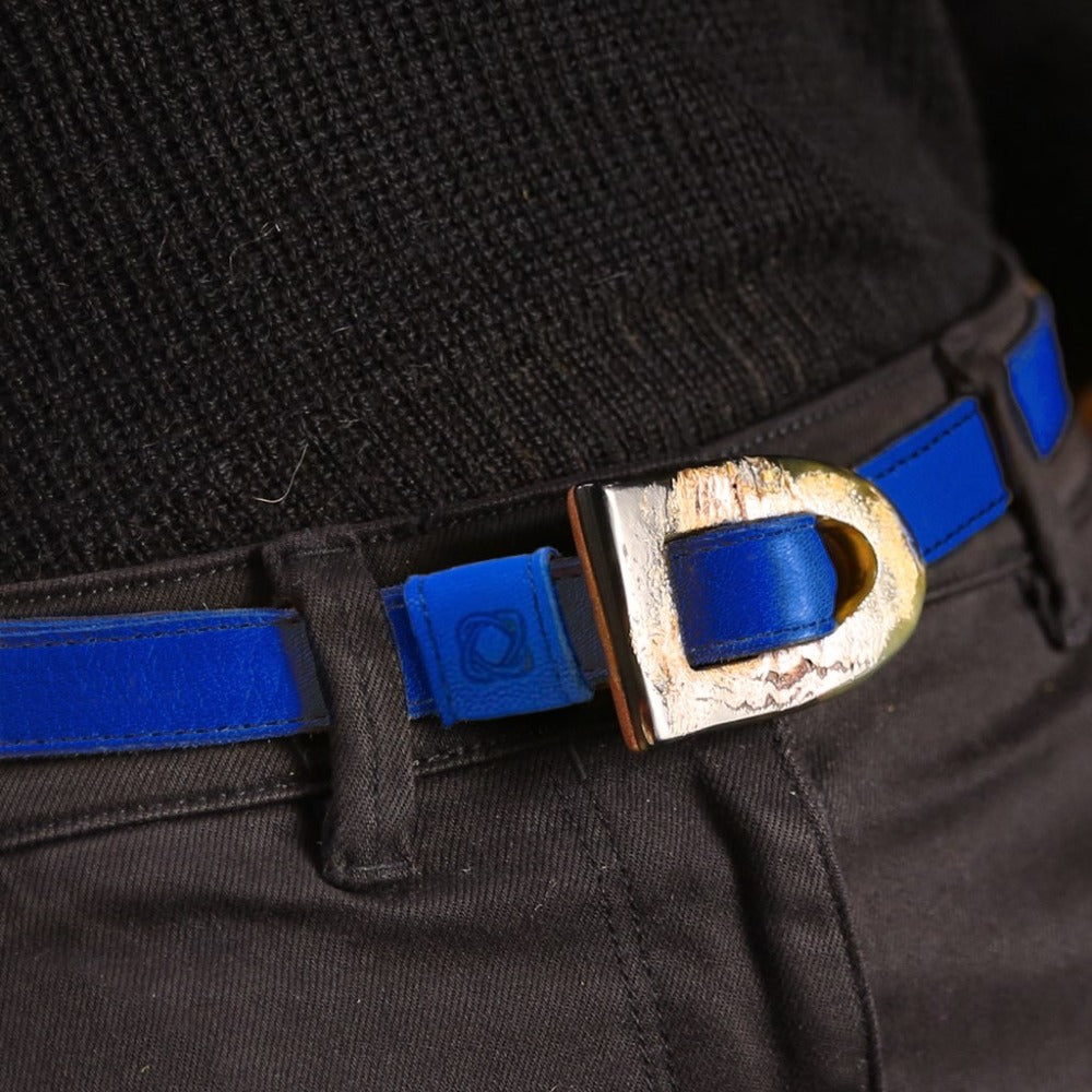 Woman wearing a blue belt, black jacket, gray top, and blue jeans with a green outdoor background