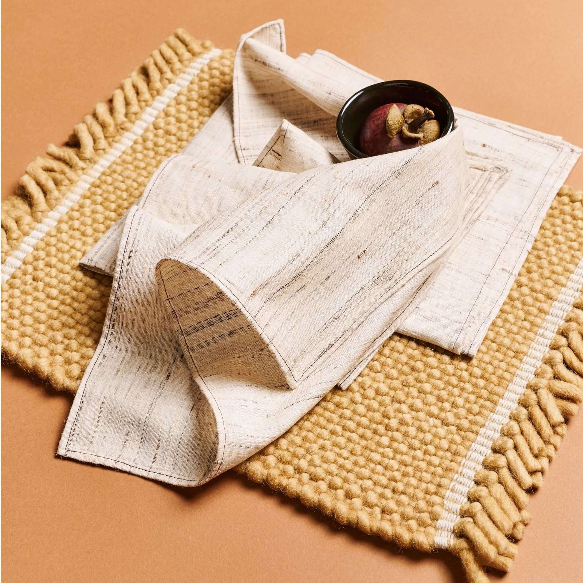 Kora Off White Peace Silk Handloom Napkin set of 4 elegantly draped on a textured mat, highlighting traditional craftsmanship.