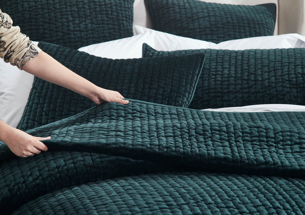 QT-363-9496_4|Hands gently touching a dark green velvet quilted bedspread, highlighting its soft, luxurious texture and cozy comfort.