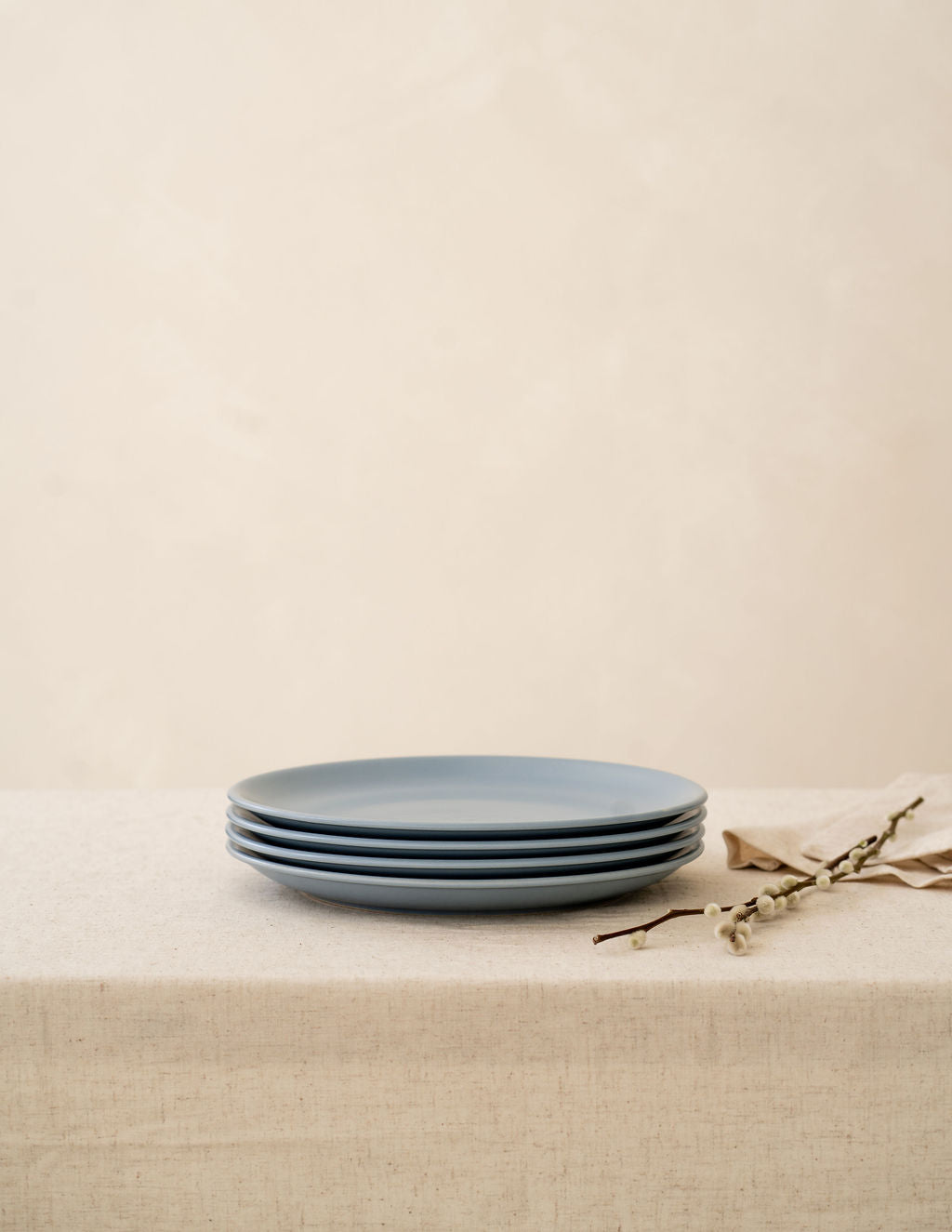 Wave blue non-toxic ceramic dinner plates from Hamkke Home stacked on a neutral linen tablecloth with floral accent.