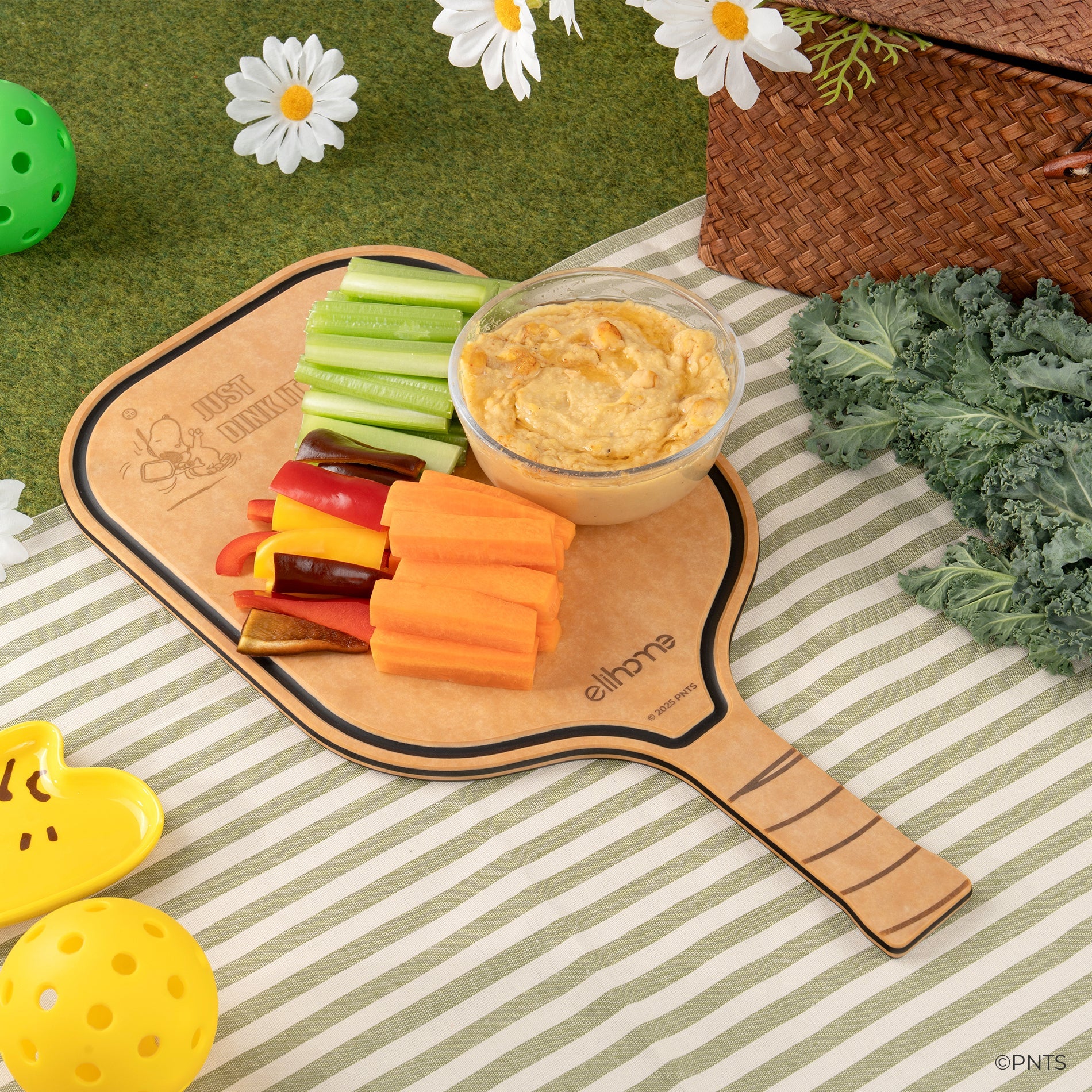 Fruit salad on a paddle-shaped cutting board with a yellow checkered tablecloth, picnic basket, and lemon on a wooden surface.