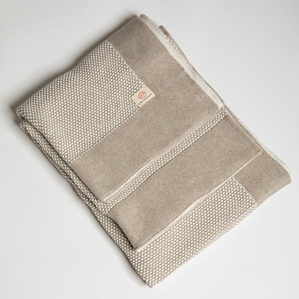 A linen sand beige and white textured cotton throw with a thick beige border folded on a plain white background. 