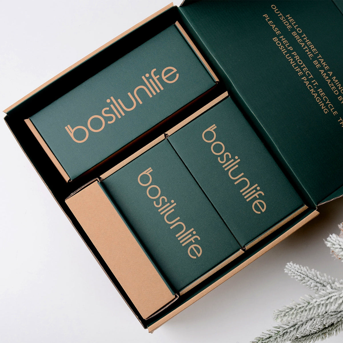 Eco-friendly premium gift packaging for the BosilunLife Nordic Garden collection, featuring an open green and kraft box with an environmental recycling message, three inner branded boxes, and styled with a frosted pine branch for holiday gifting.