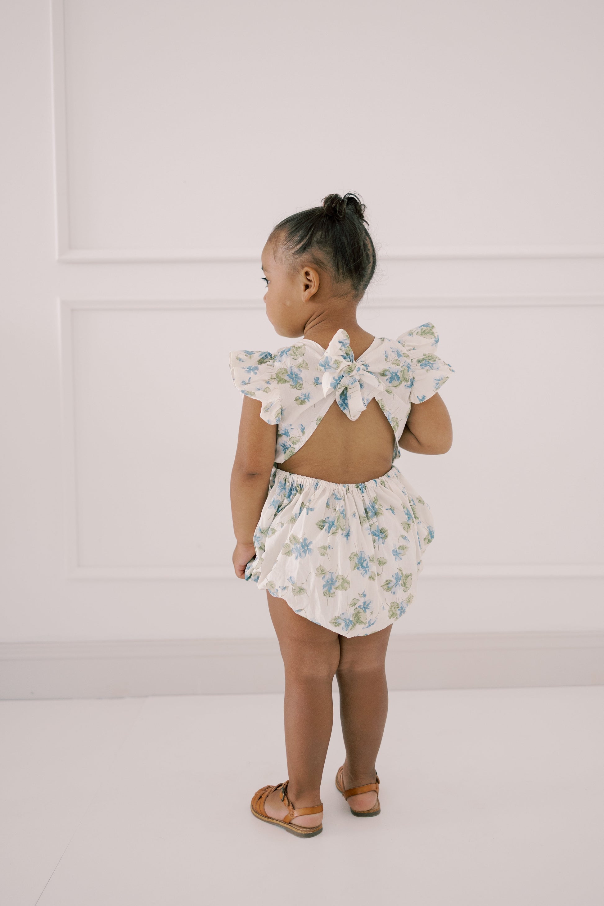 Child wearing a floral romper  with tied back bow back closure