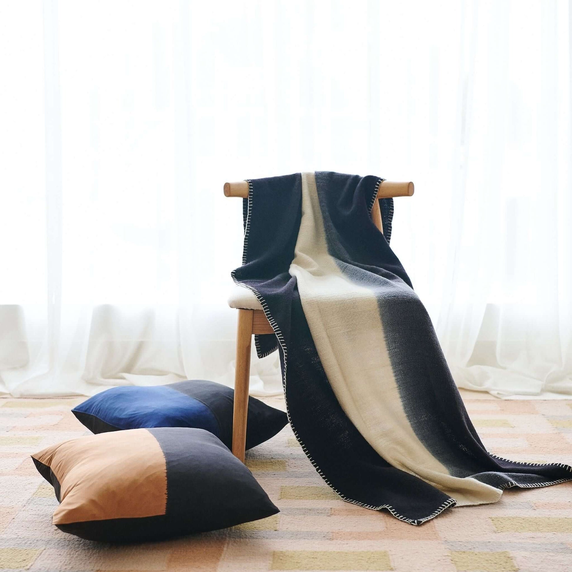 Ink Black White Ombre Textured Throw In Hand Spun Merino And Hand Stitched Hem draped over a chair with decorative pillows.