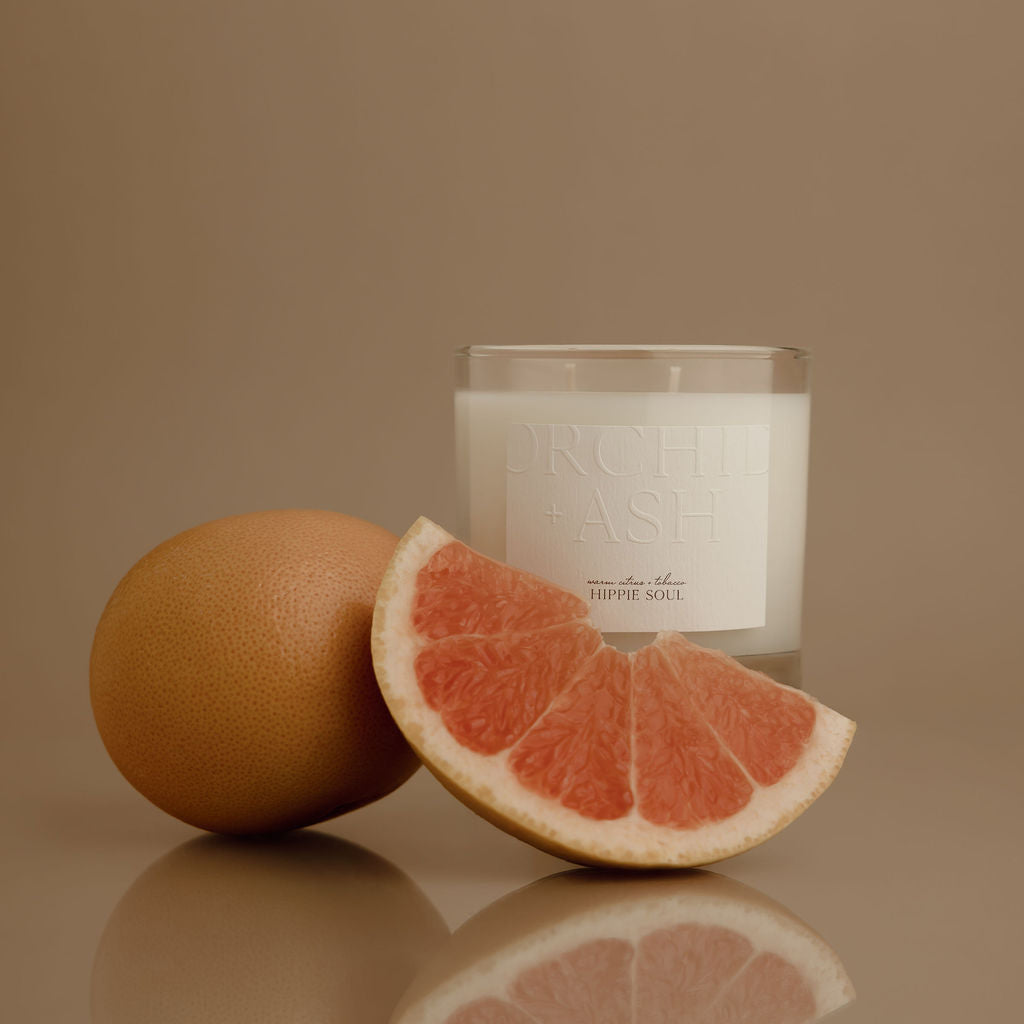 Candle with a grapefruit slice and whole grapefruit on a reflective surface against a brown background
