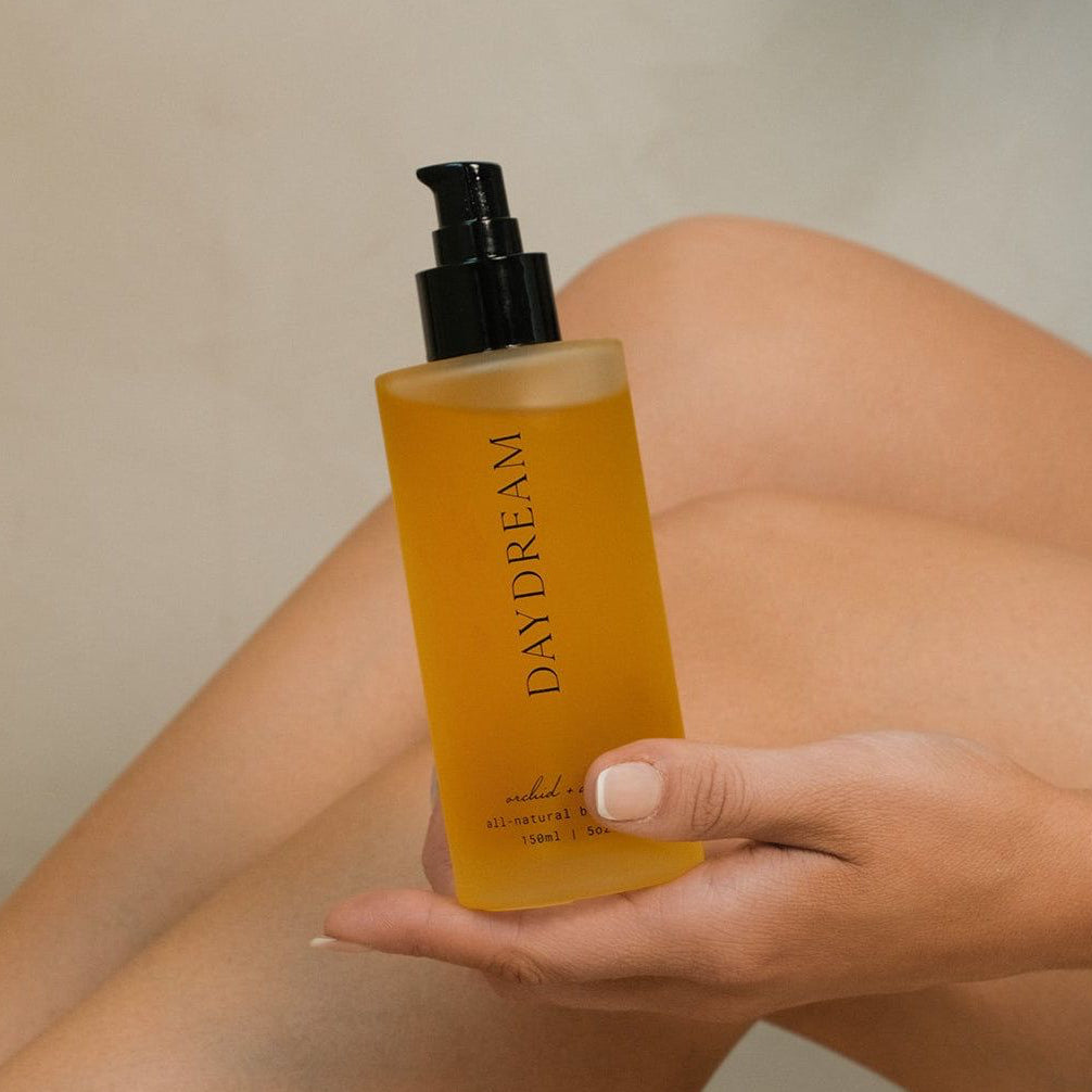 Hand holding a bottle of 'Daydream' product against a neutral background