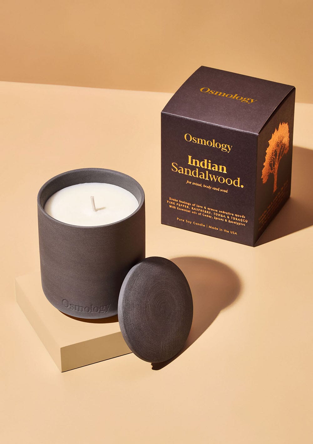 Osmology black ceramic indian sandalwood scented candle displayed next to decorative product packaging on white background