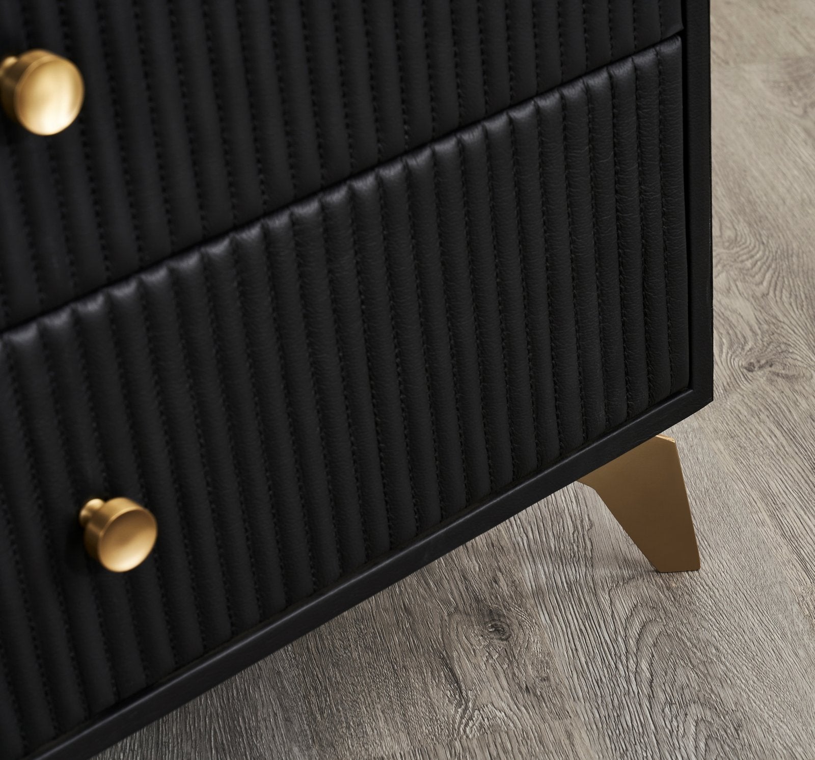 FN-5202-262028_9|Detailed view of black leather nightstand's bottom drawers, showing vertical tufting and chic gold tapered legs. Contemporary furniture item.