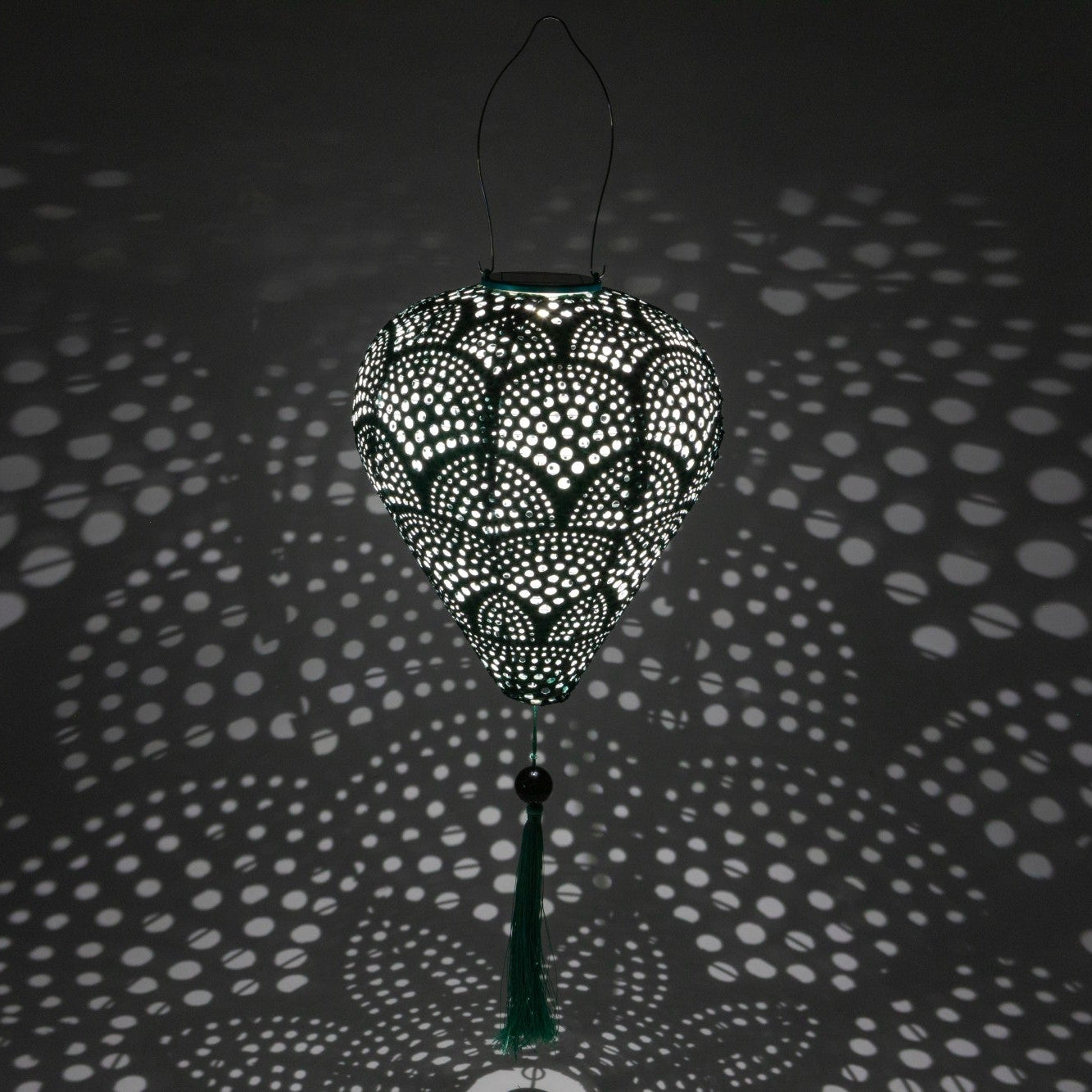 Decorative hanging lamp with intricate patterns casting shadows on a dark background