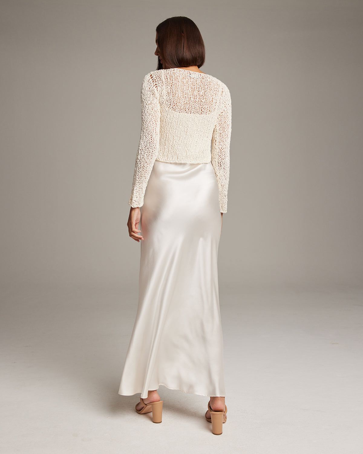 Model wearing a Flammé Loose Knit Cropped Sweater, back view, paired with a satin skirt.