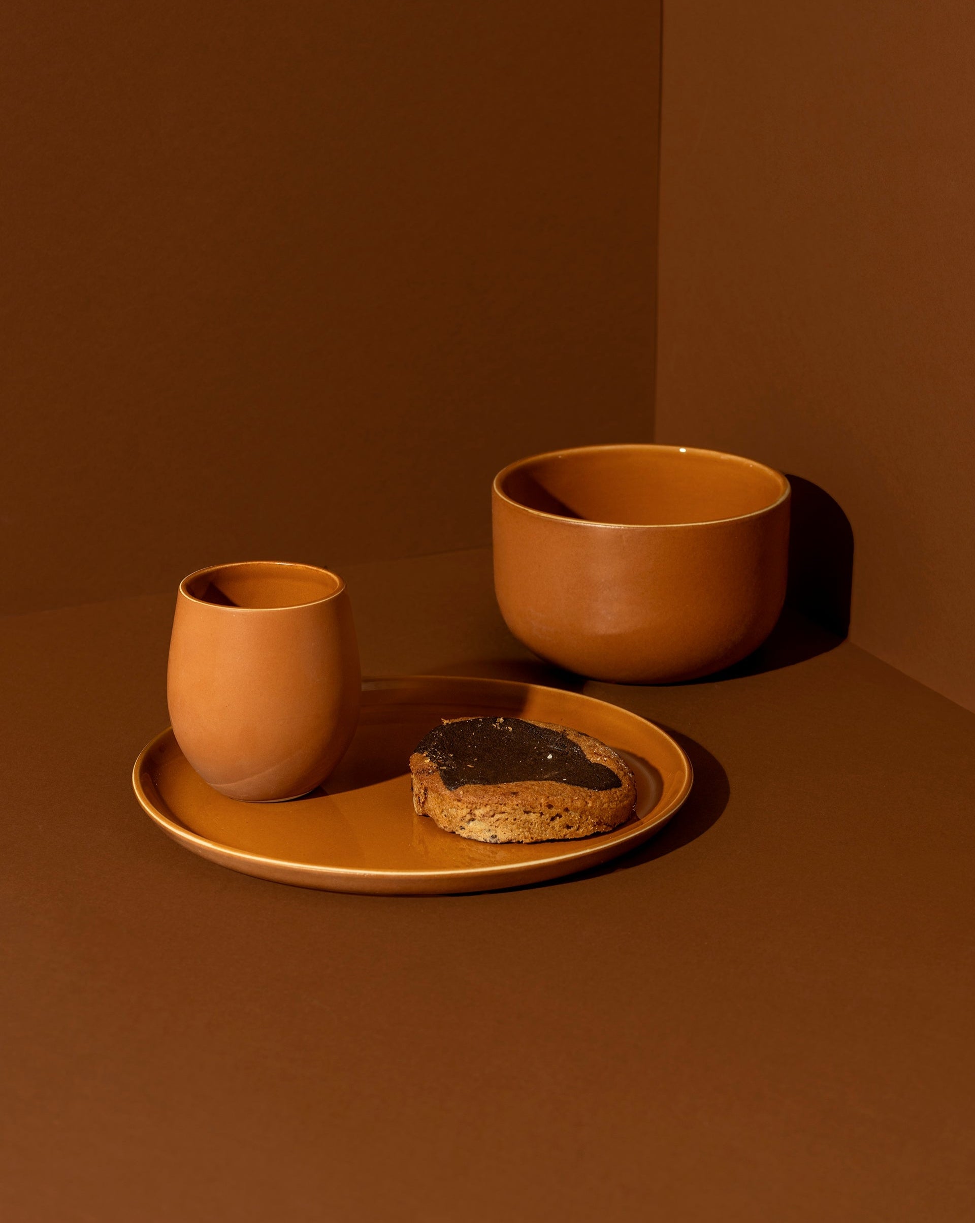 A minimalist white dinnerware set displayed against a neutral background, including a flat salad plate with a dessert, a dinner bowl, and a cup.