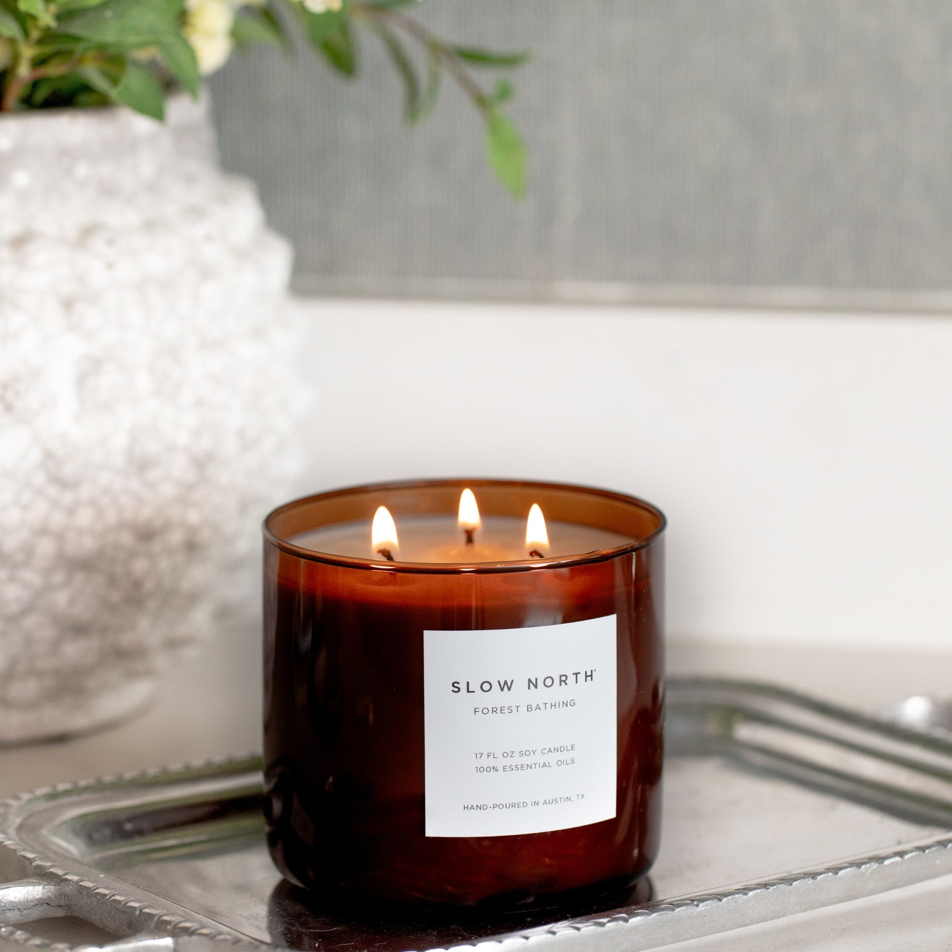 Brown 3-wick soy candle with a label on a reflective surface, with a blurred background