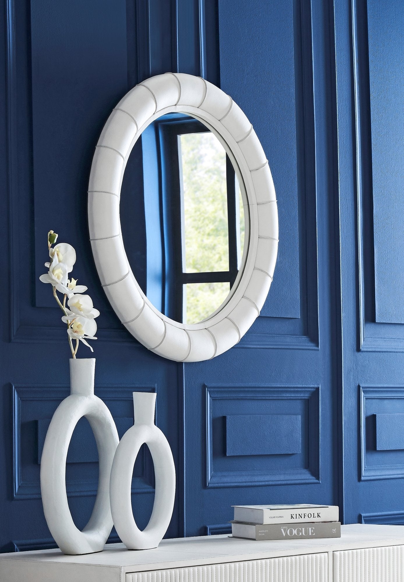 FN-5202-X-4_1|Elegant round wall mirror featuring a textured white frame, reflecting a window, mounted on a chic navy blue paneled wall.
