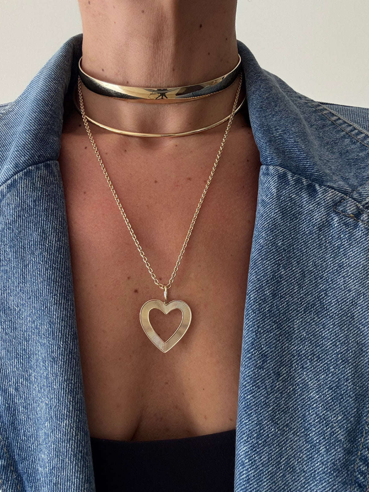 Three gold necklaces featuring a wide choker, delicate choker, and long heart pendant