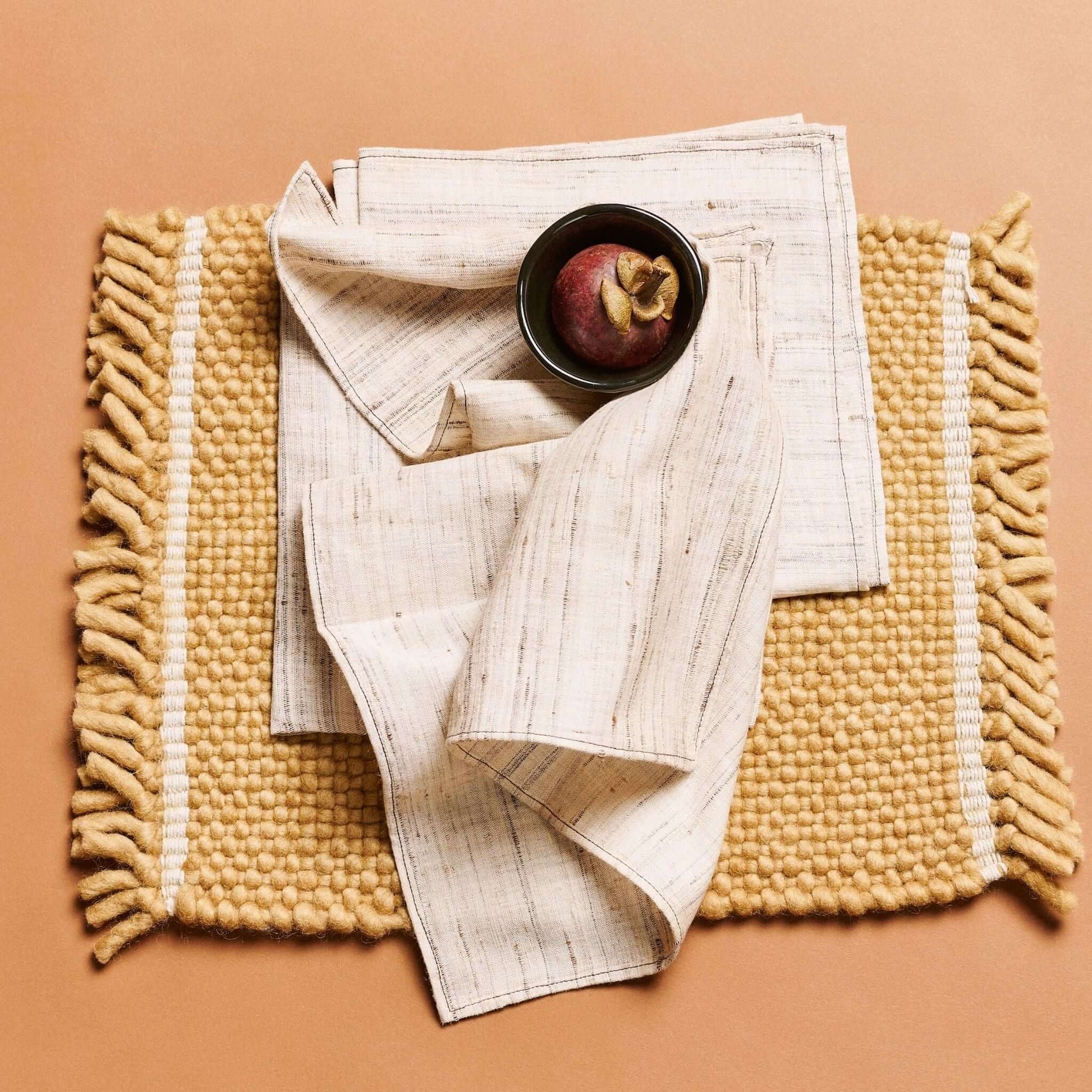 Kora Off White Peace Silk Handloom Napkin set of 4 on a textured backdrop, featuring a bowl and fruit.