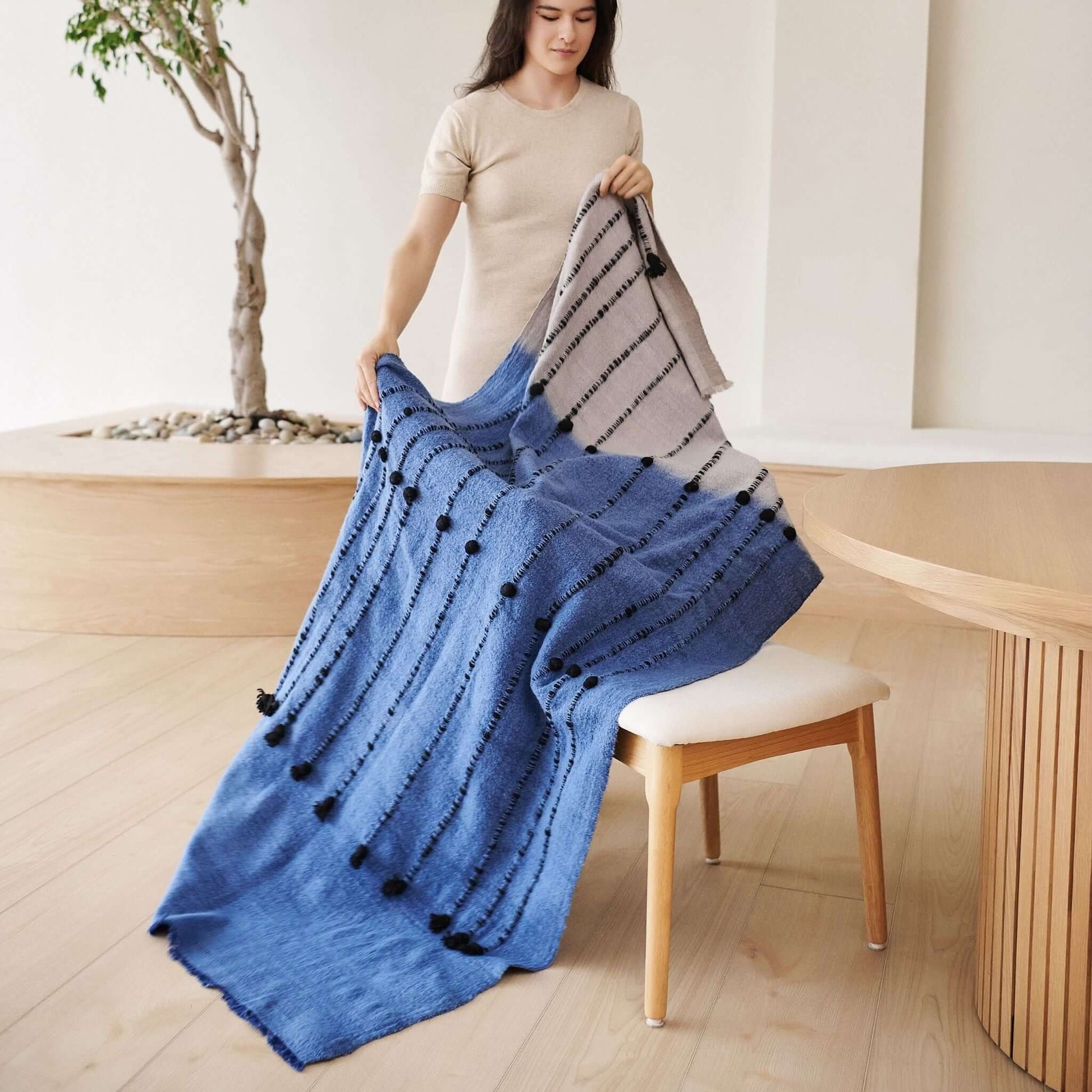 Hand Knotted Merino Textured Mari Throw Blanket in Blue Gray displayed by a model in a cozy interior setting.